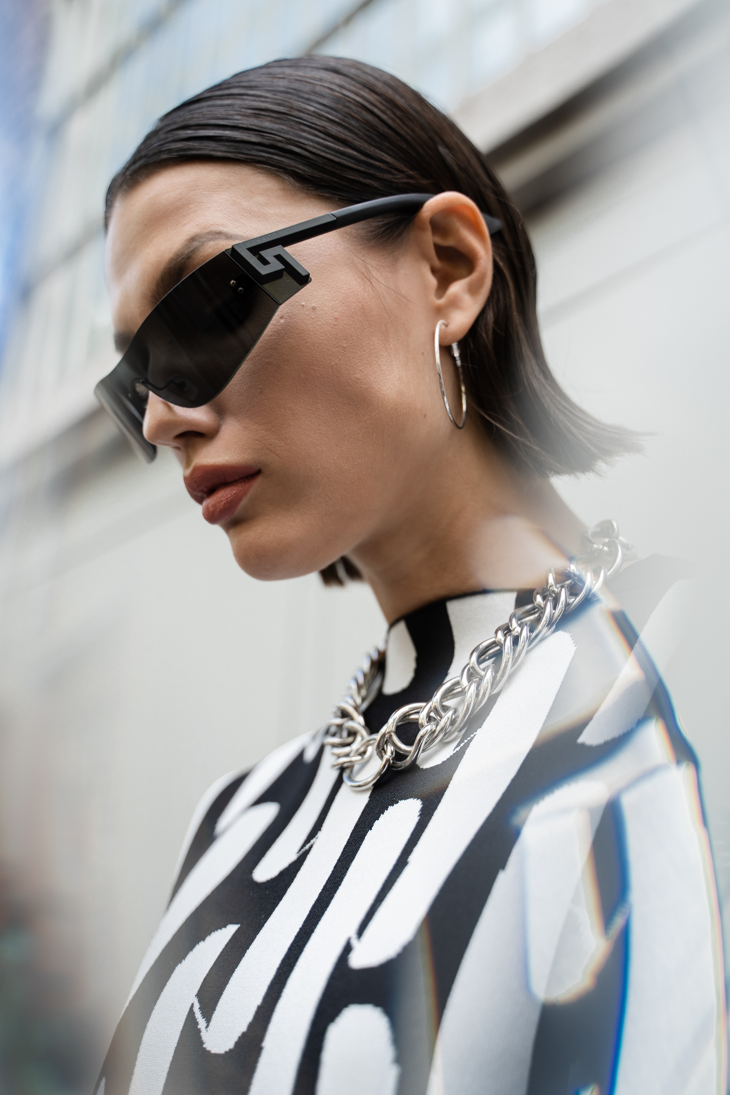 Portrait of a woman wearing dark sunglasses and a silver chain necklace reflecting city lights