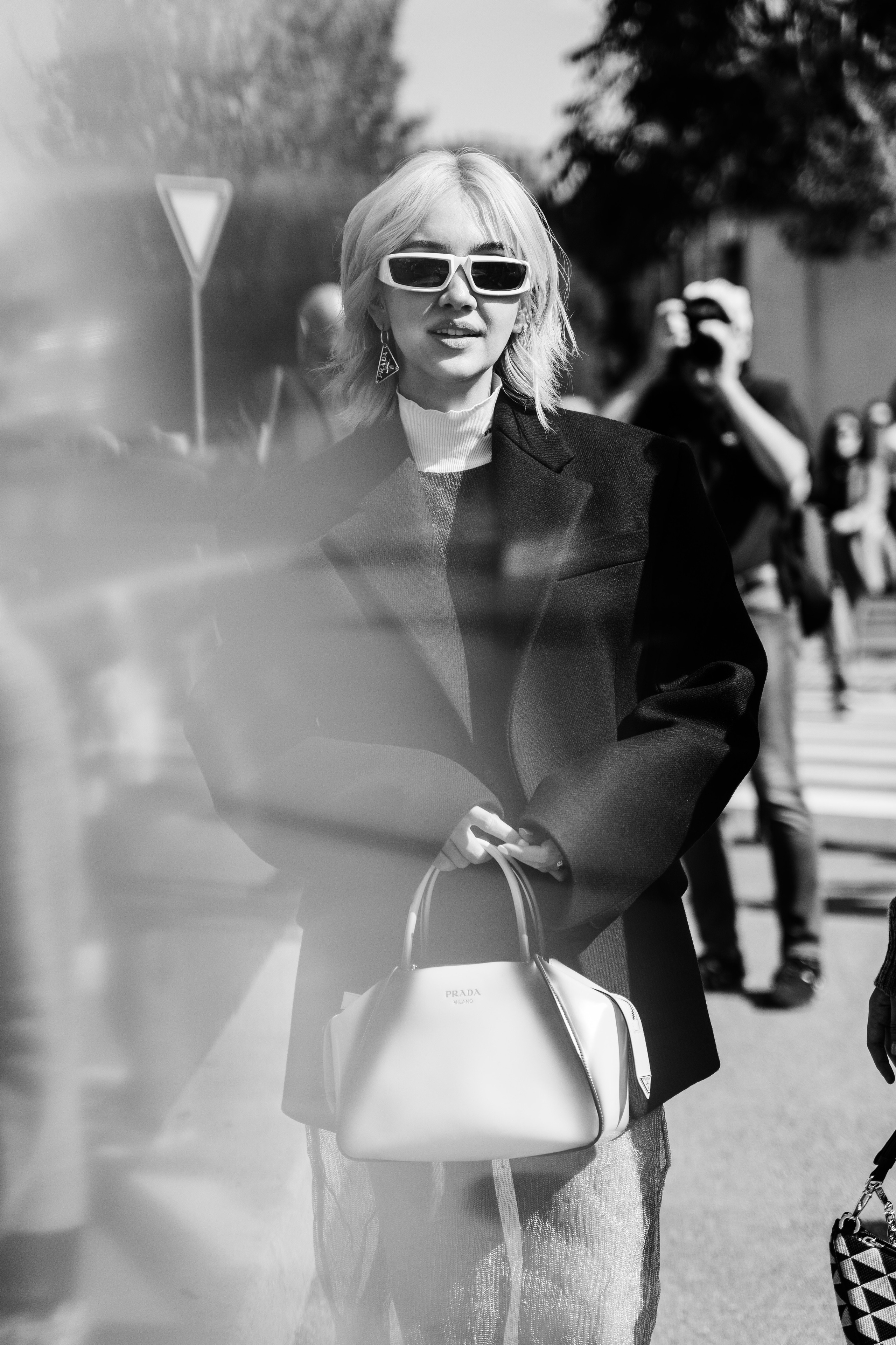 Stylish blonde woman in oversized black blazer with feather details at Milan Fashion Week