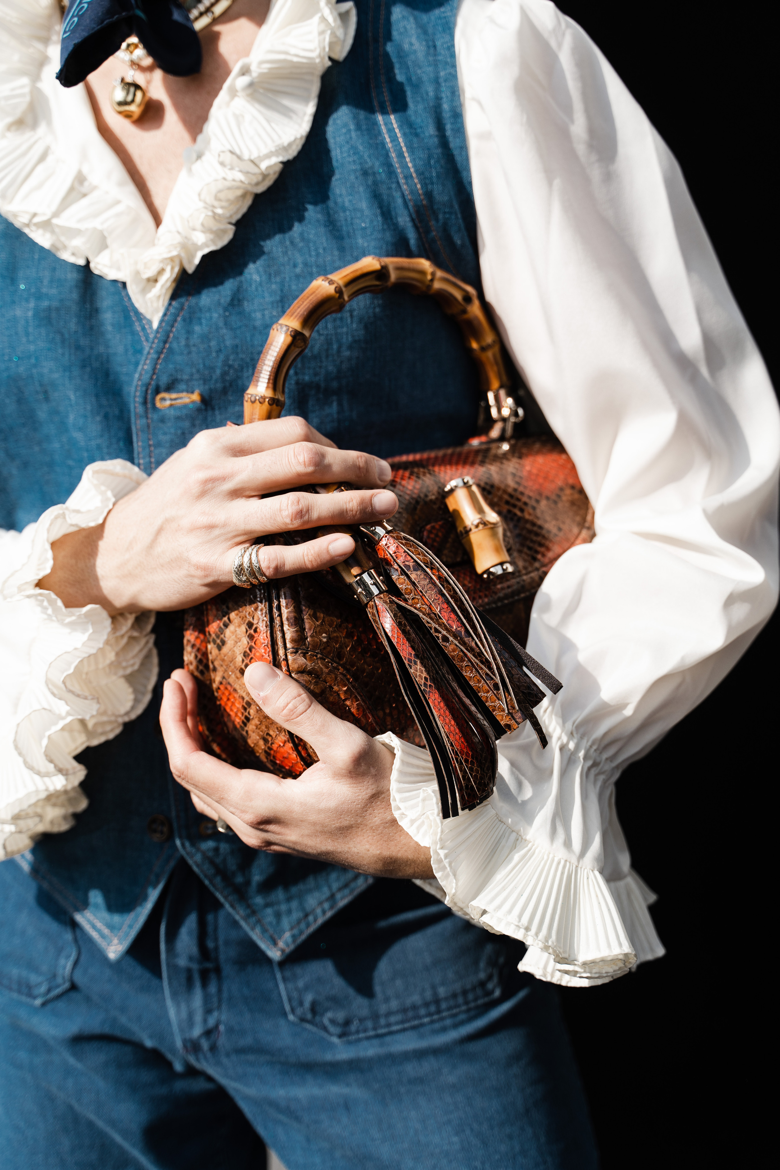 Close-up of a man’s hands adorned with rings, holding a designer python leather handbag