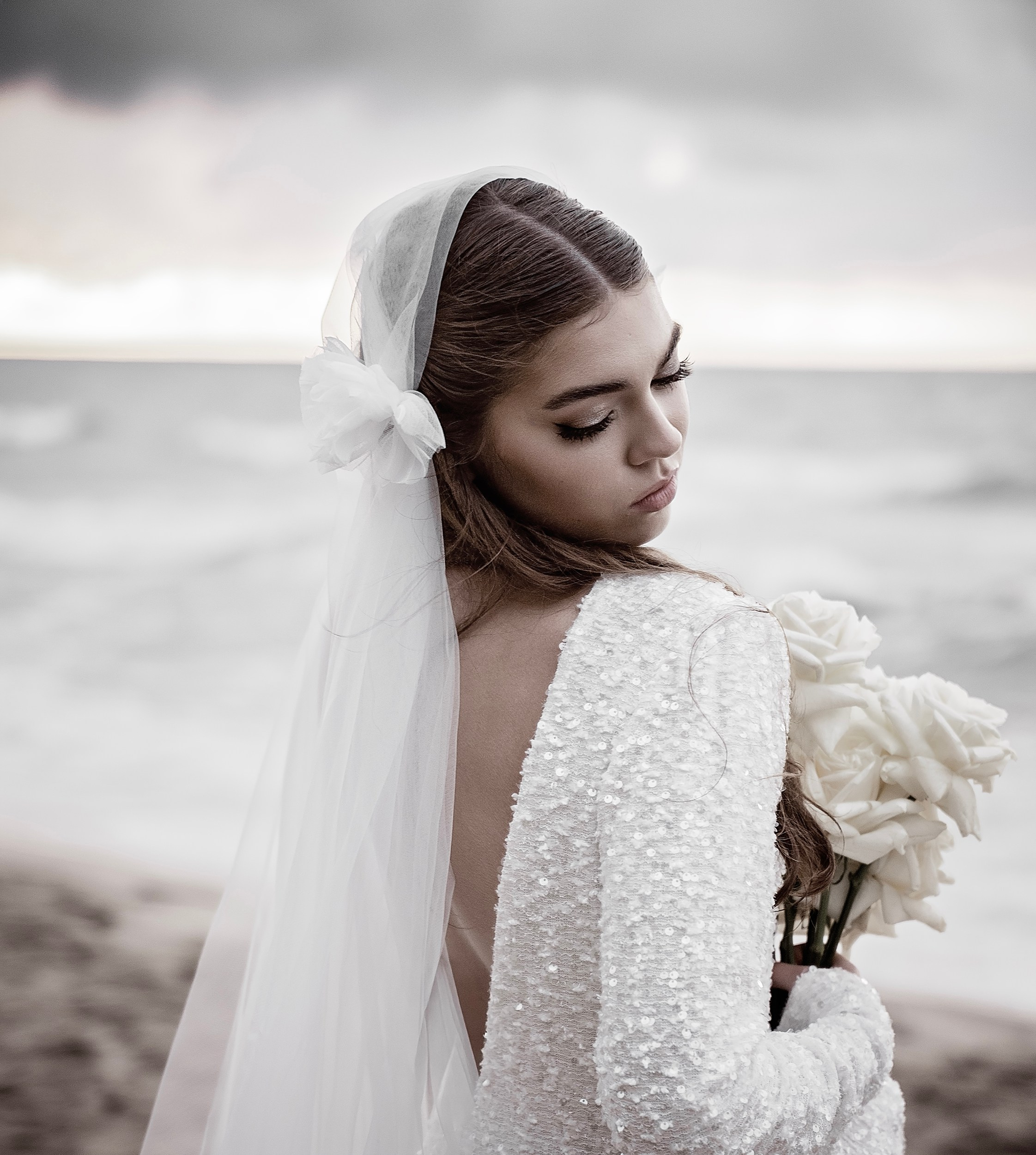 Close-up portrait of a bride with a long wedding veil holding a bouquet on the beach. Romantic coastal wedding photography in Ireland.
