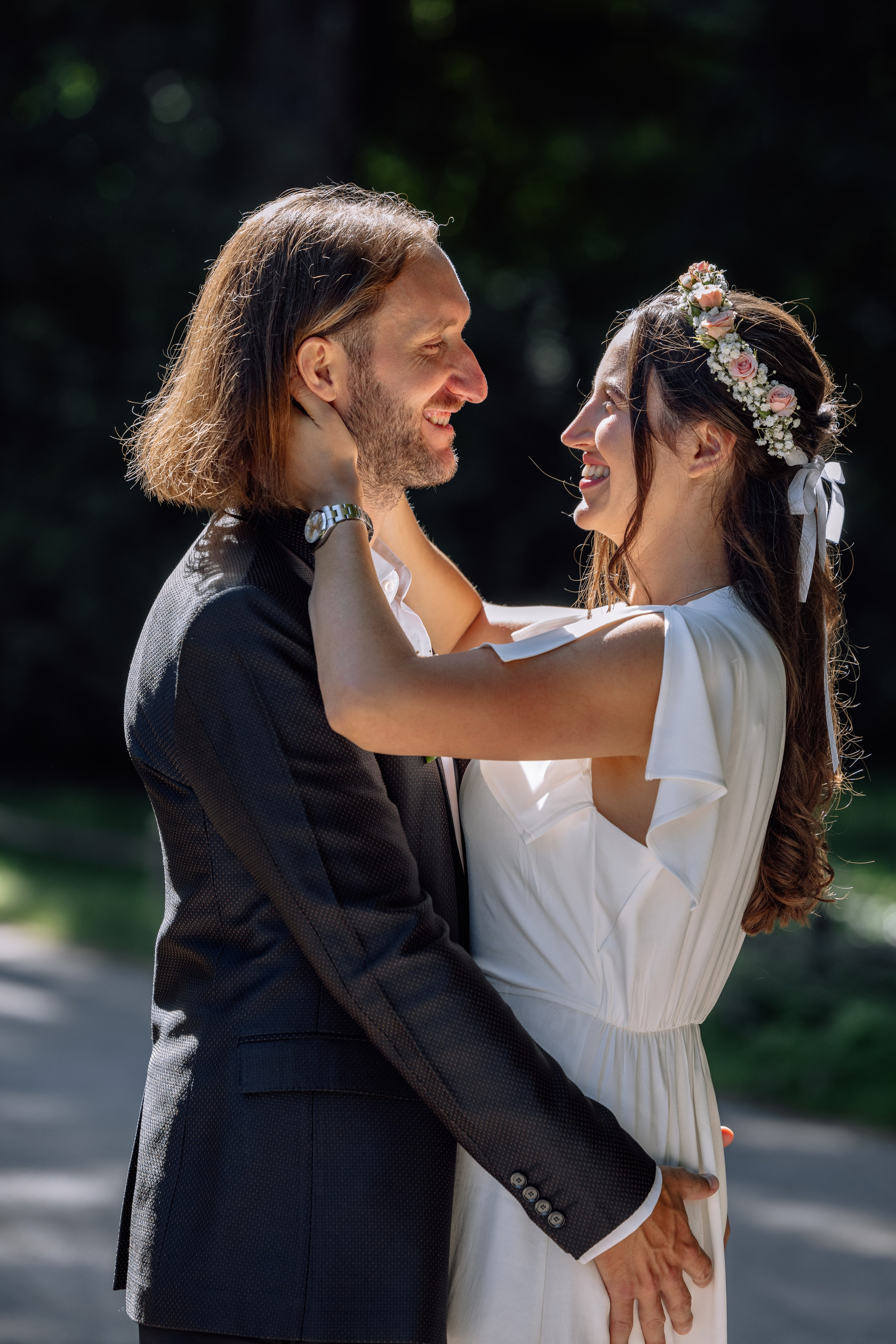 Brautpaar hält Hände, berührt sanft das Gesicht des Partners – Spaziergang im Englischen Garten