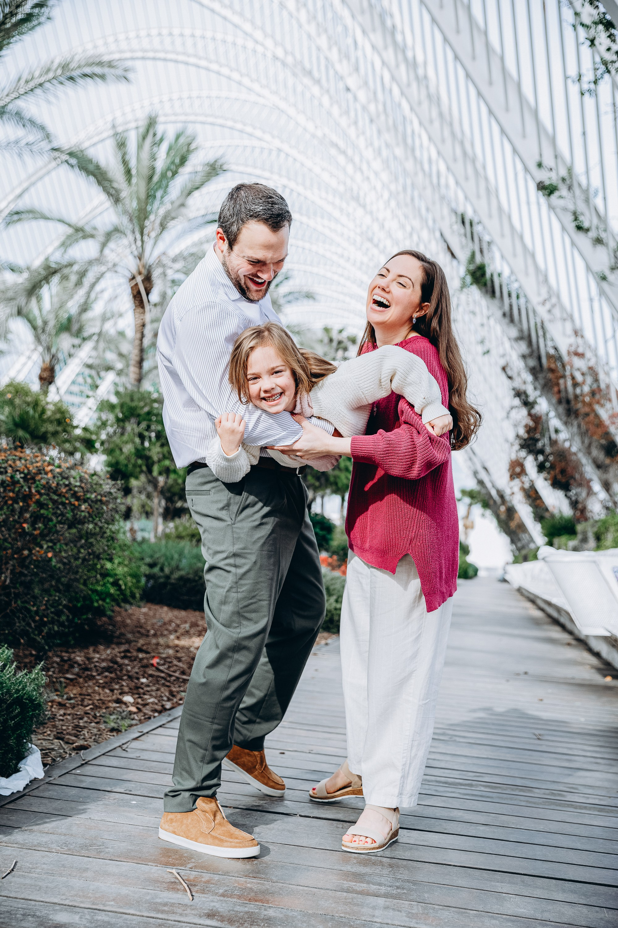 Семейная фотосессия в Валенсии, Испания, где родители держат своего ребёнка, гуляя вместе по живописной дорожке, снято при естественном свете для тёплого, искреннего и близкого семейного момента — идеально для семейных фотосессий в Валенсии и по всей Испании.