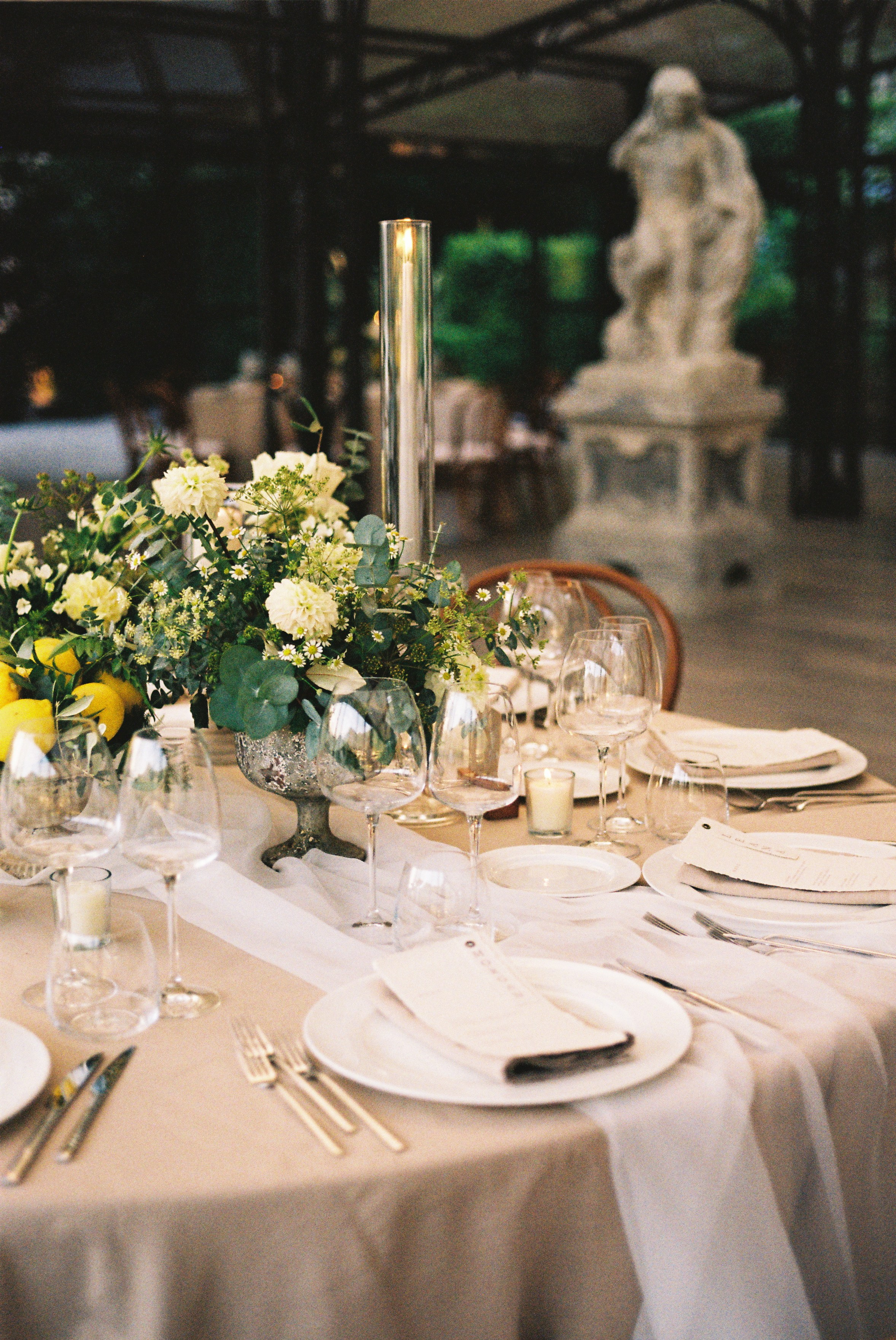 Wedding table setting with floral arrangement, candles, and fine dinnerware, under soft evening light.