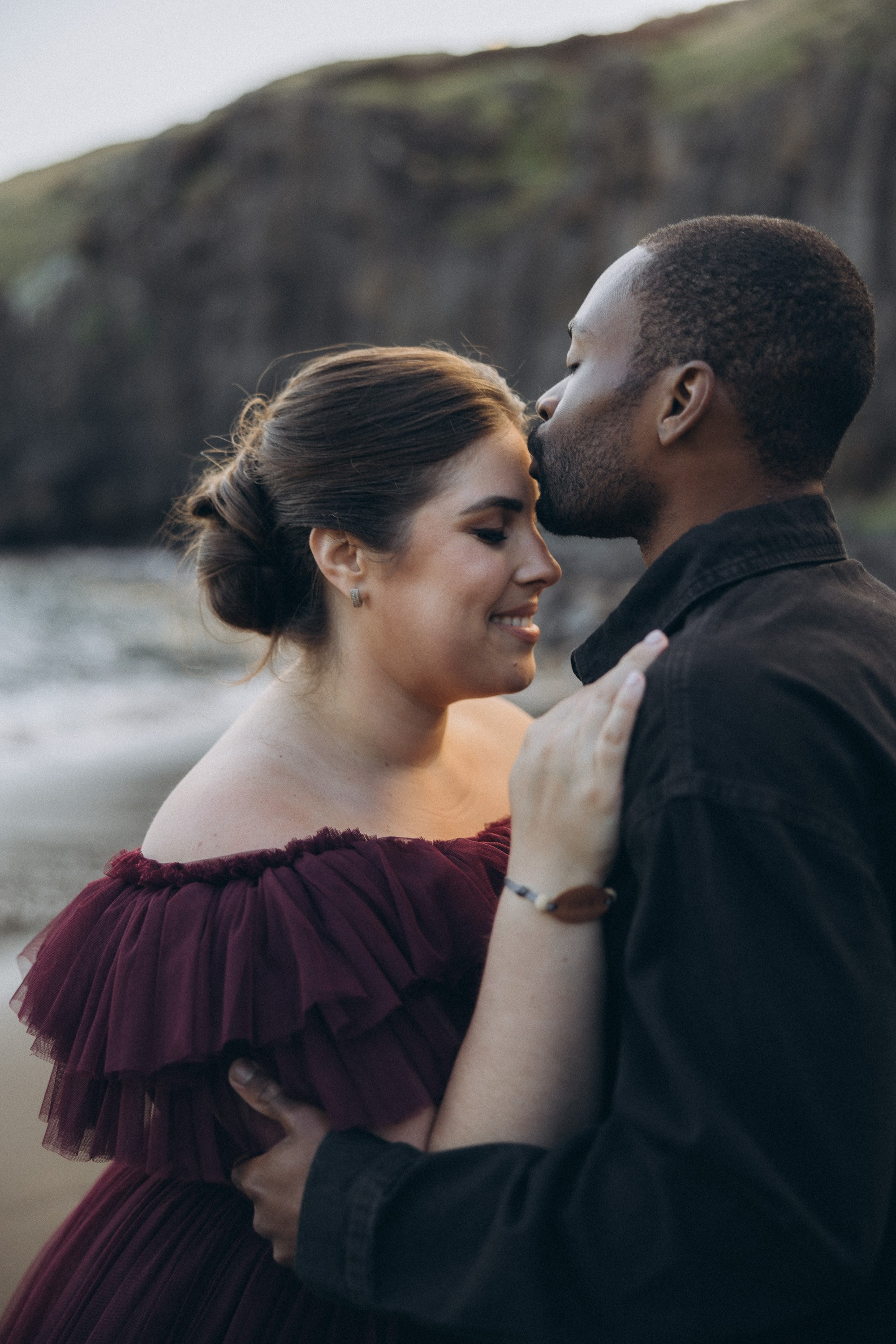 A glowing expectant mother standing on a cliff overlooking the ocean in Madeira, her dress flowing gently in the wind as the golden sunset casts a warm glow.