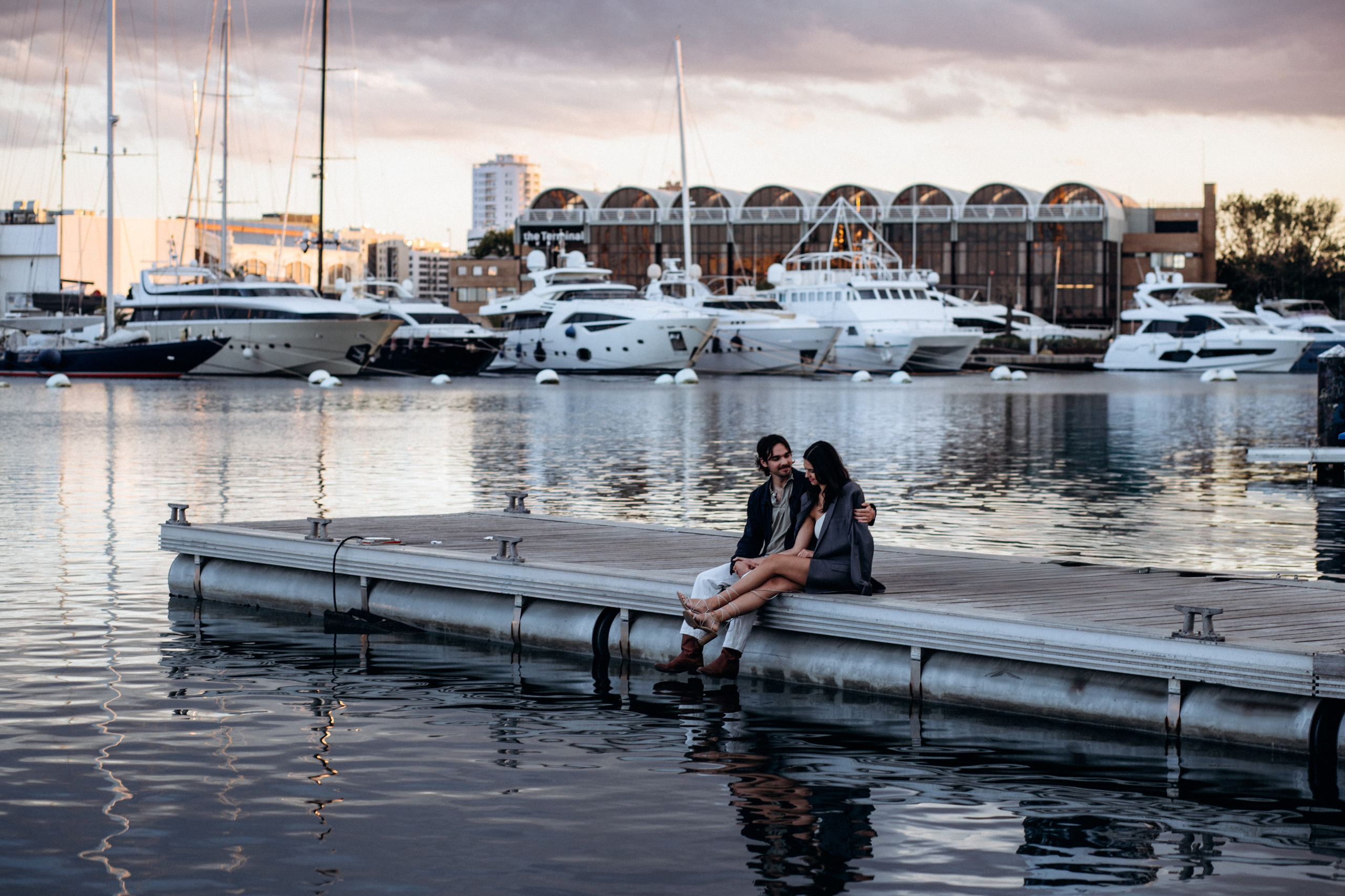 Romantic couple photoshoot at the marina in Valencia, Spain — capturing a candid moment of love and connection by the water with luxury yachts in the background, perfect for those searching for love story or couple photography sessions in Valencia and coastal Spain.