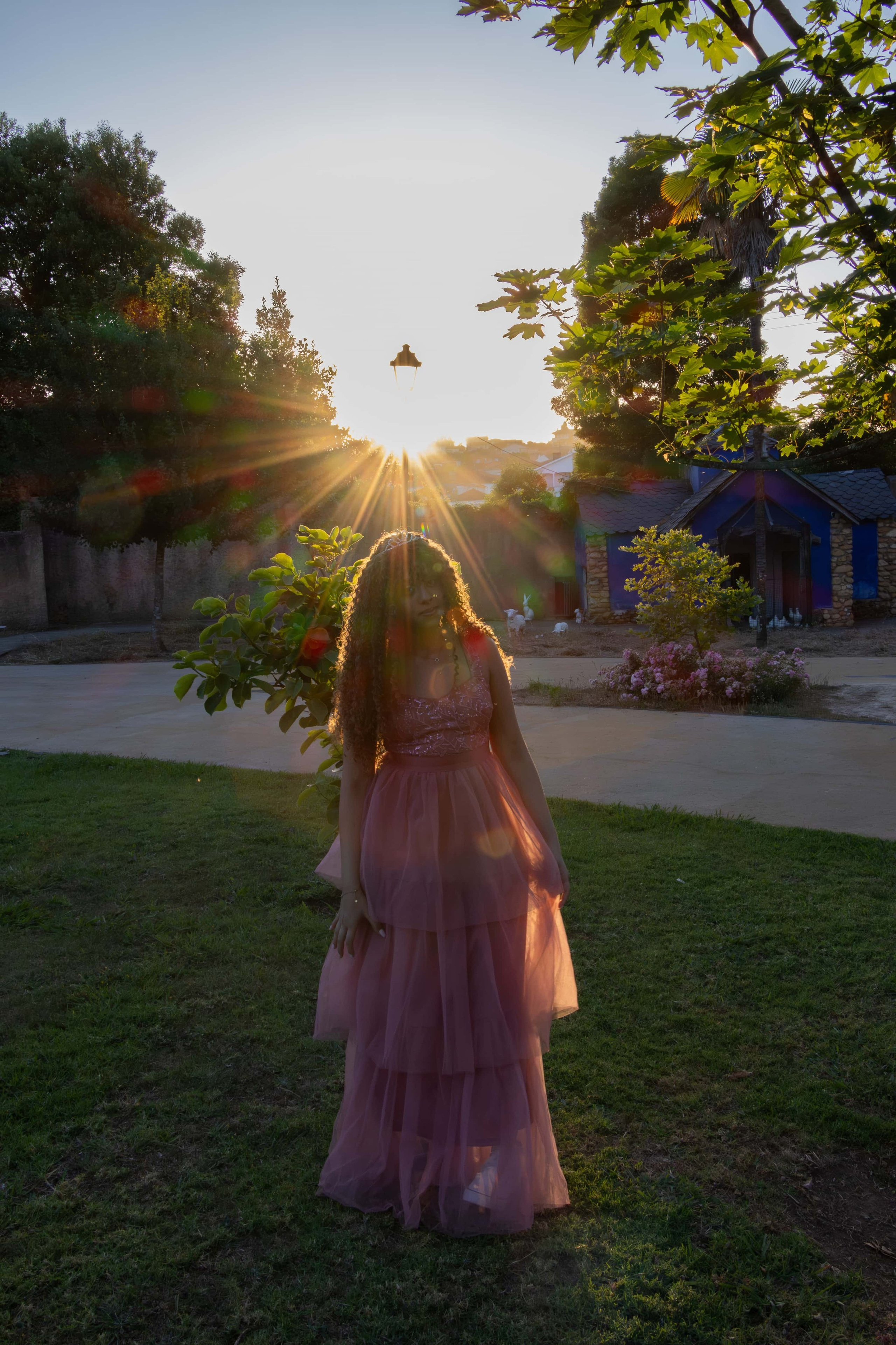 Fotografia contra a luz (silhueta) de uma jovem caminhando em um campo ao pôr do sol, com o brilho solar criando um efeito de lens flare dourado.