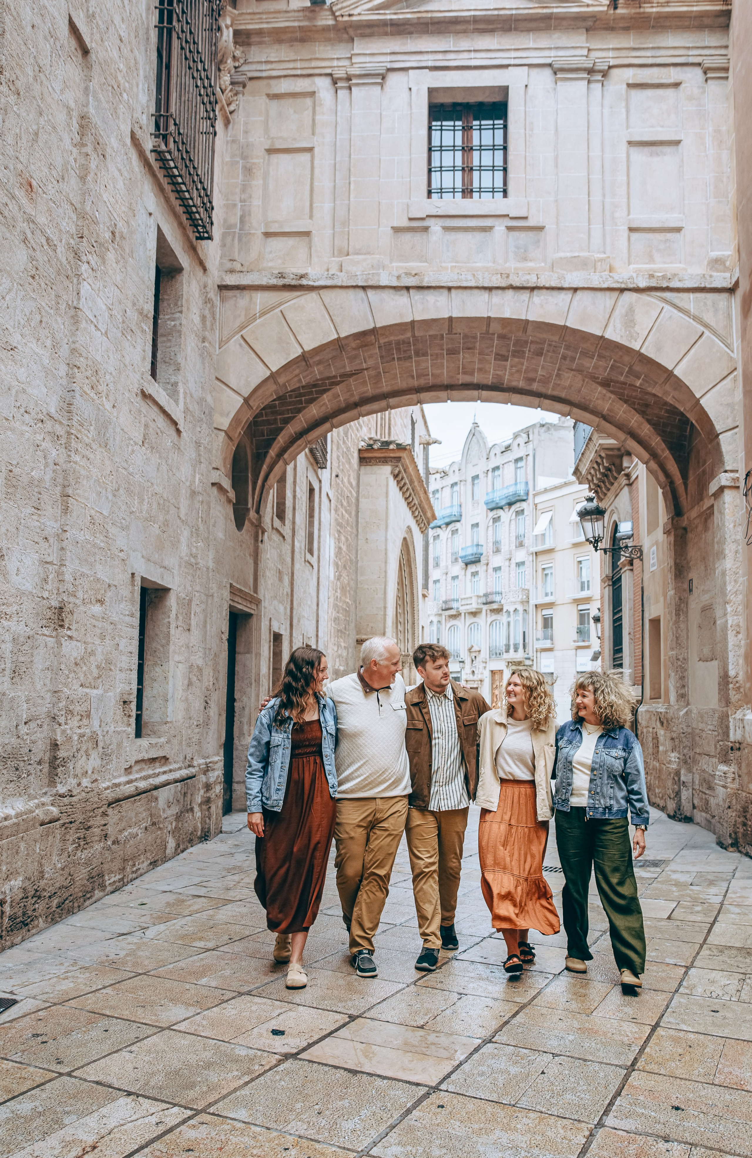 Foto espontánea de una familia caminando bajo un arco histórico en el corazón de Valencia, España — perfecta para quienes buscan sesiones familiares naturales y artísticas en Valencia y en toda España. Inspiración ideal para fotografía urbana familiar con encanto europeo.