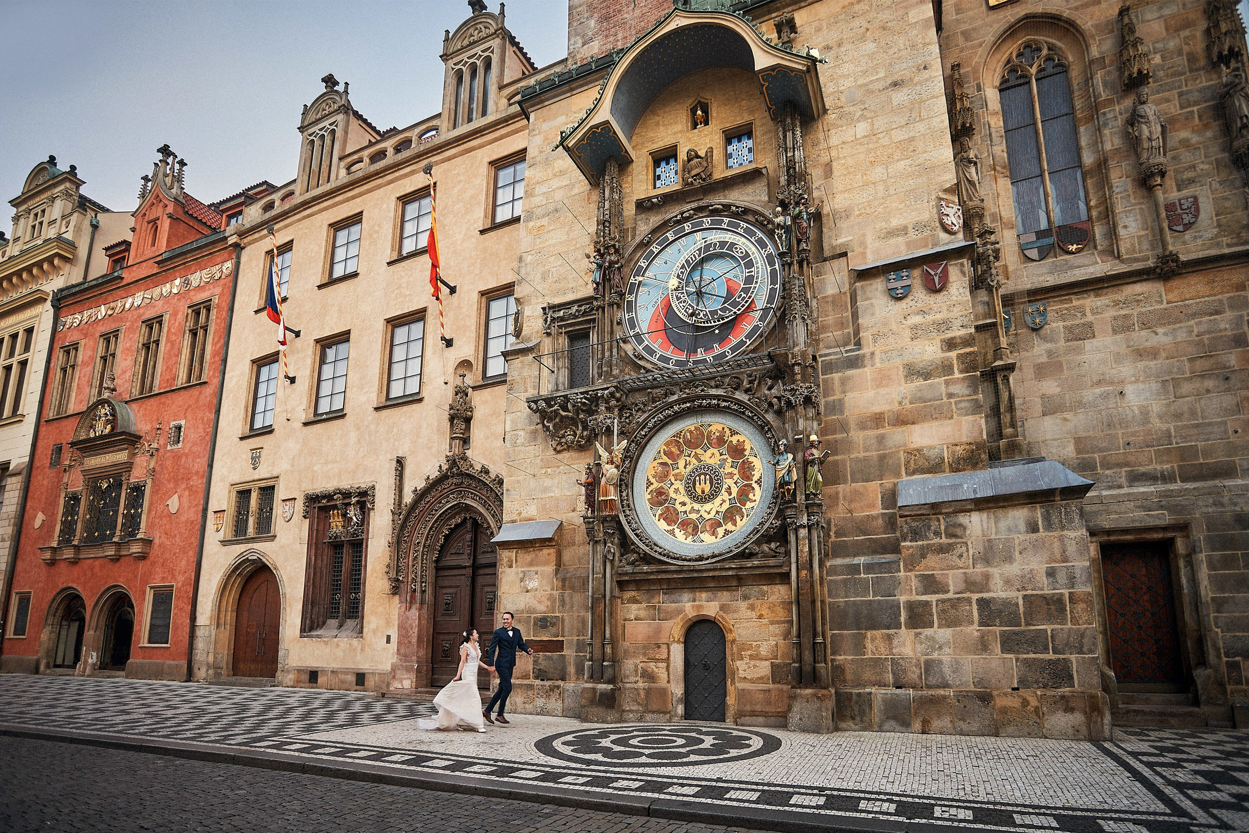 Asian bride runs hand-in-hand with her groom underneath the towering Astronomical Clock in Prague 