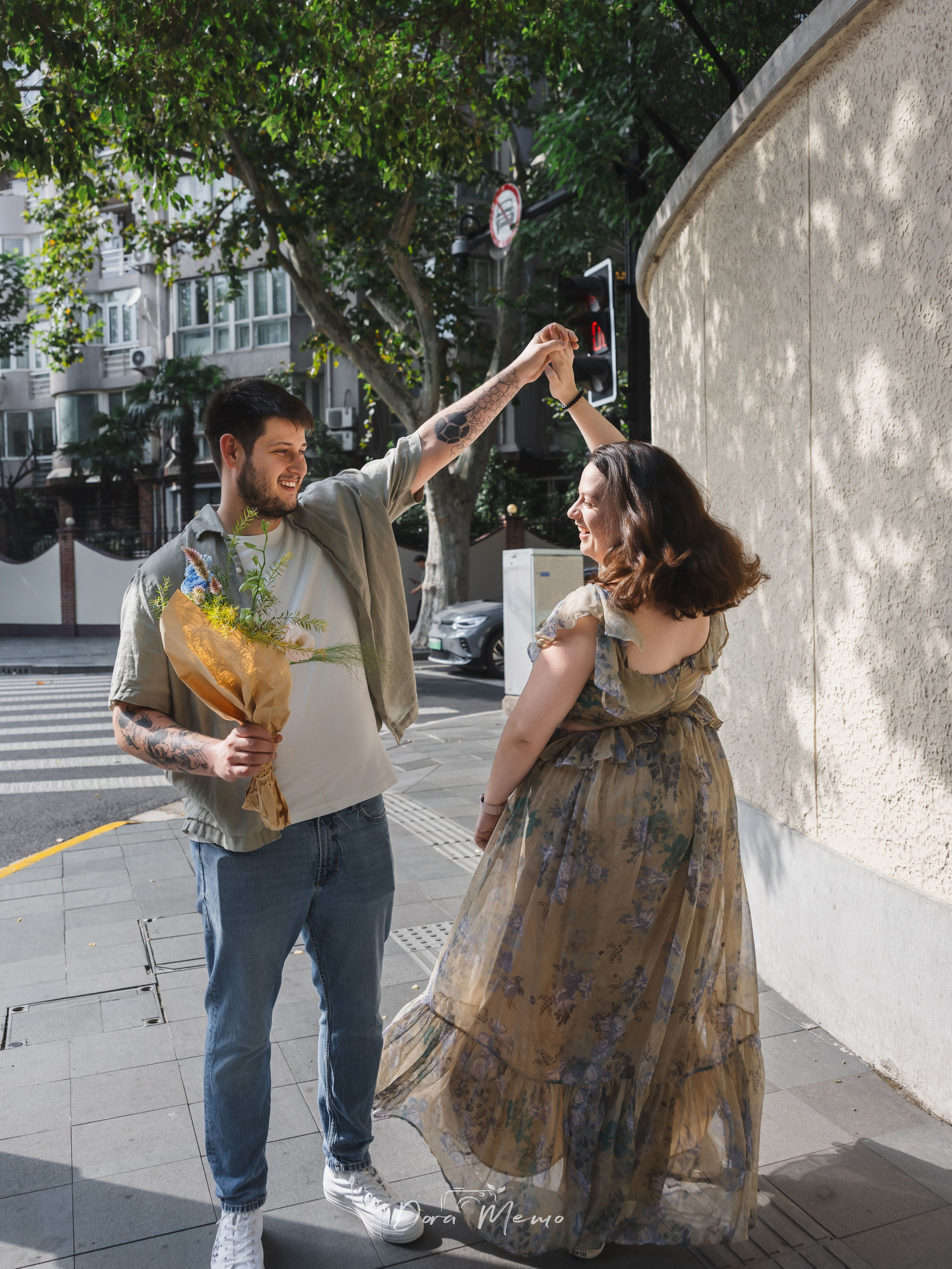 A playful street portrait of a couple walking together with flowers under Shanghai plane trees.