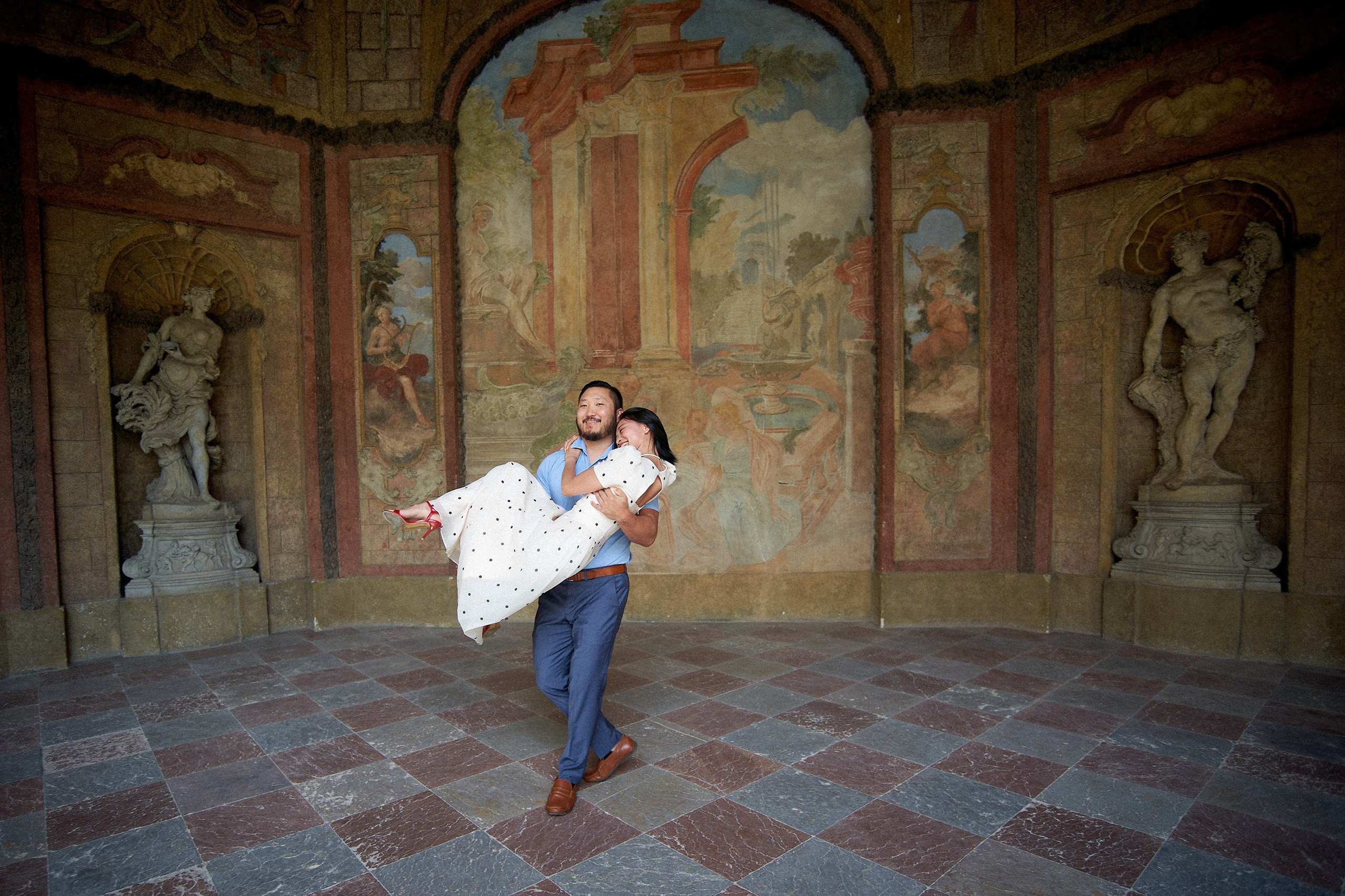 Man carrying his fiancée in his arms as they exit the Sala Terrena in Vrtba Garden, Prague.