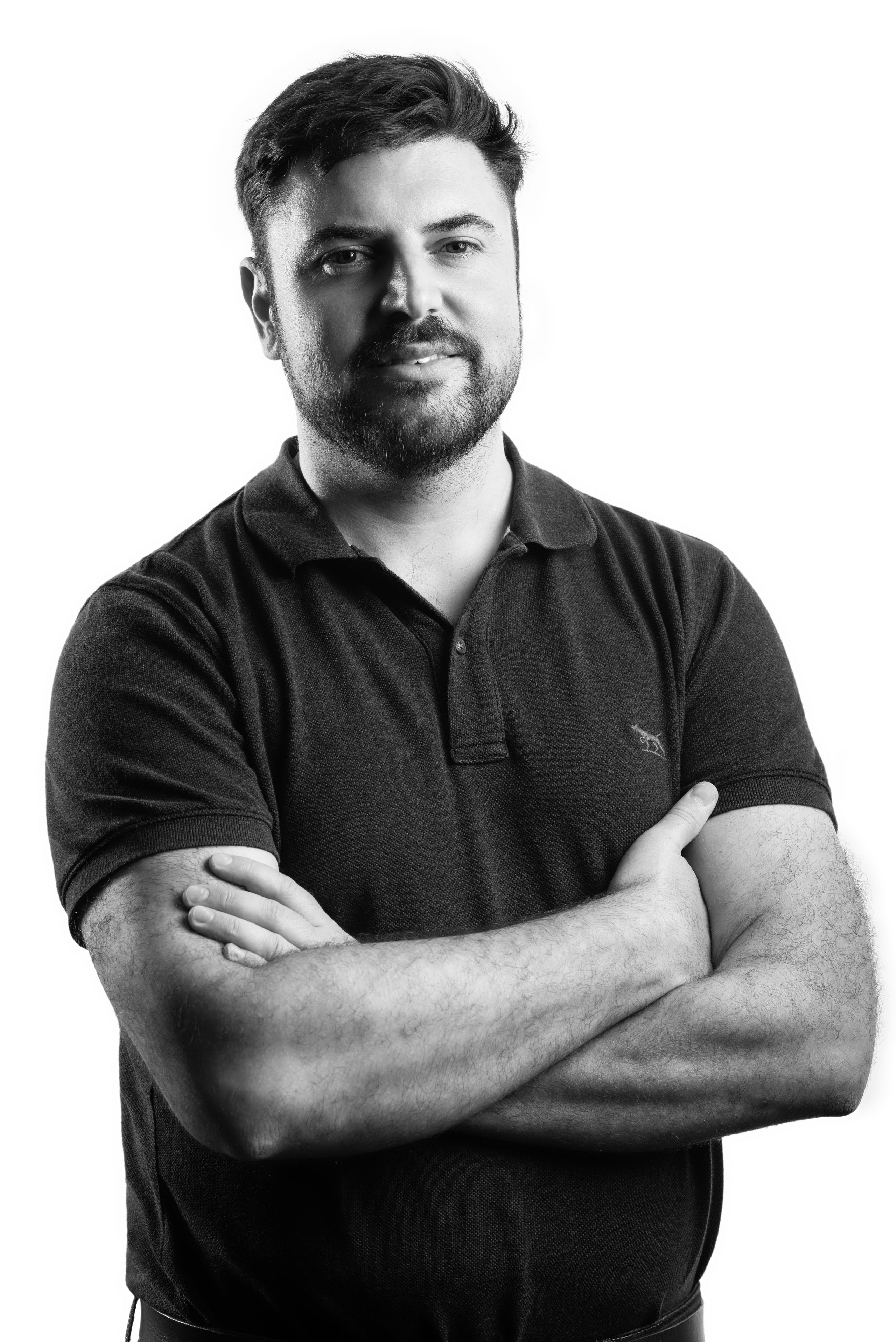 A black-and-white corporate portrait of a confident man with a beard, wearing a dark polo shirt and crossing his arms. The subject is photographed against a bright white background, emphasizing his strong and approachable presence. This image highlights professional portrait photography designed for corporate branding and team profiles, tailored to businesses in Singapore seeking impactful, high-quality visuals.
