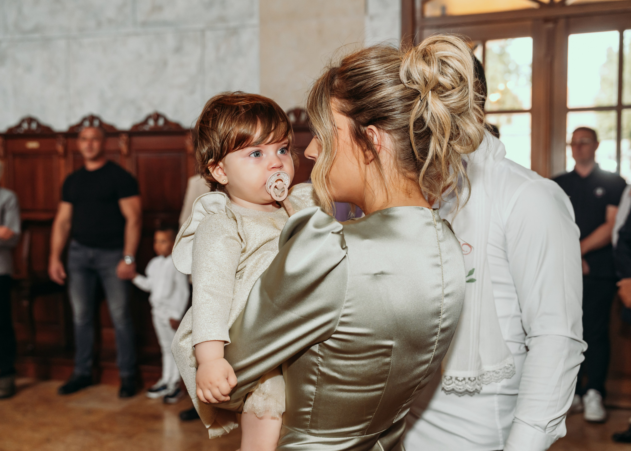 Mama drzi devojcicu u haljini tokom krstenja