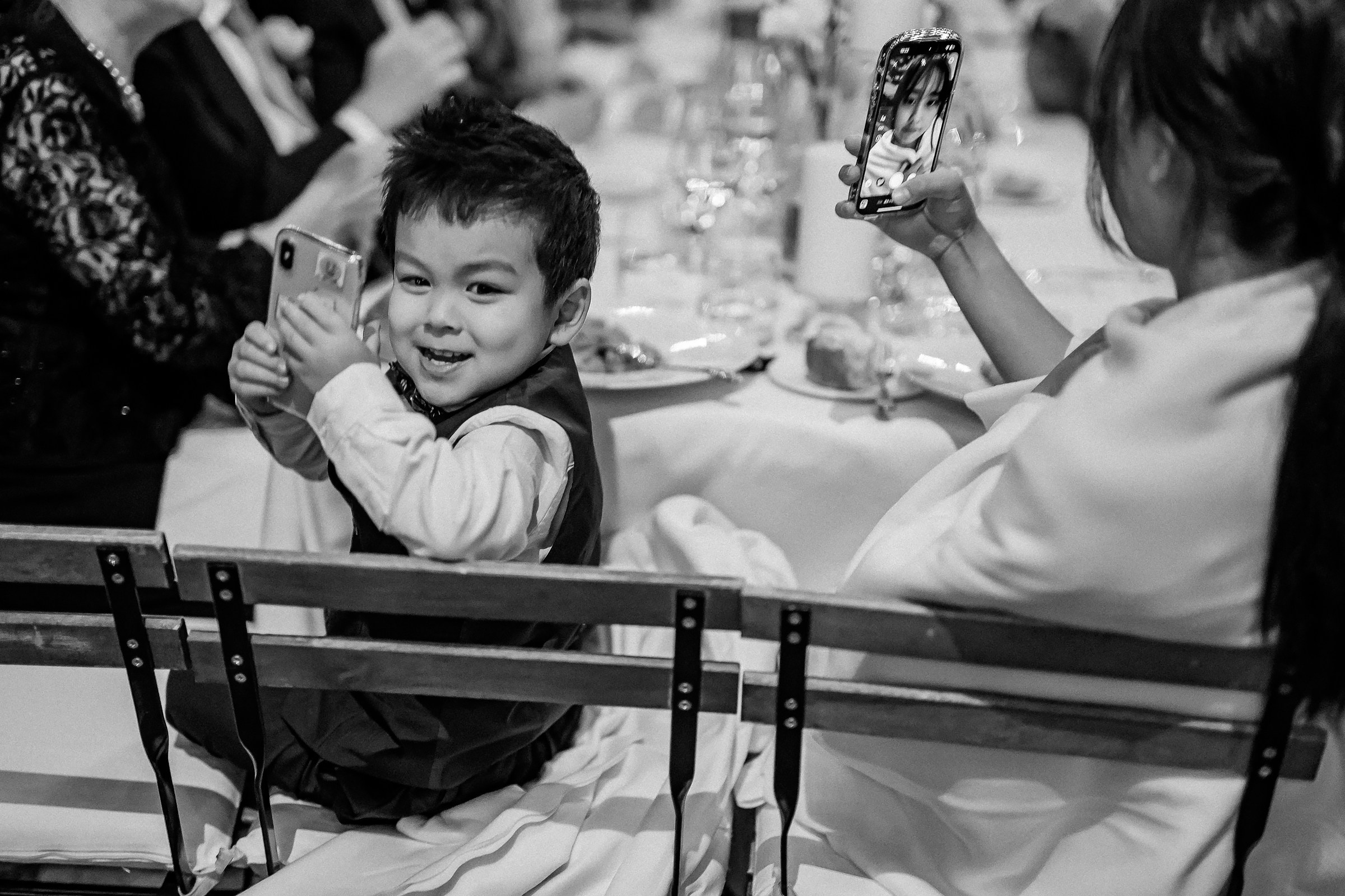 Smiling young boy holds a phone, mimicking the adults around him capturing memories on their devices.