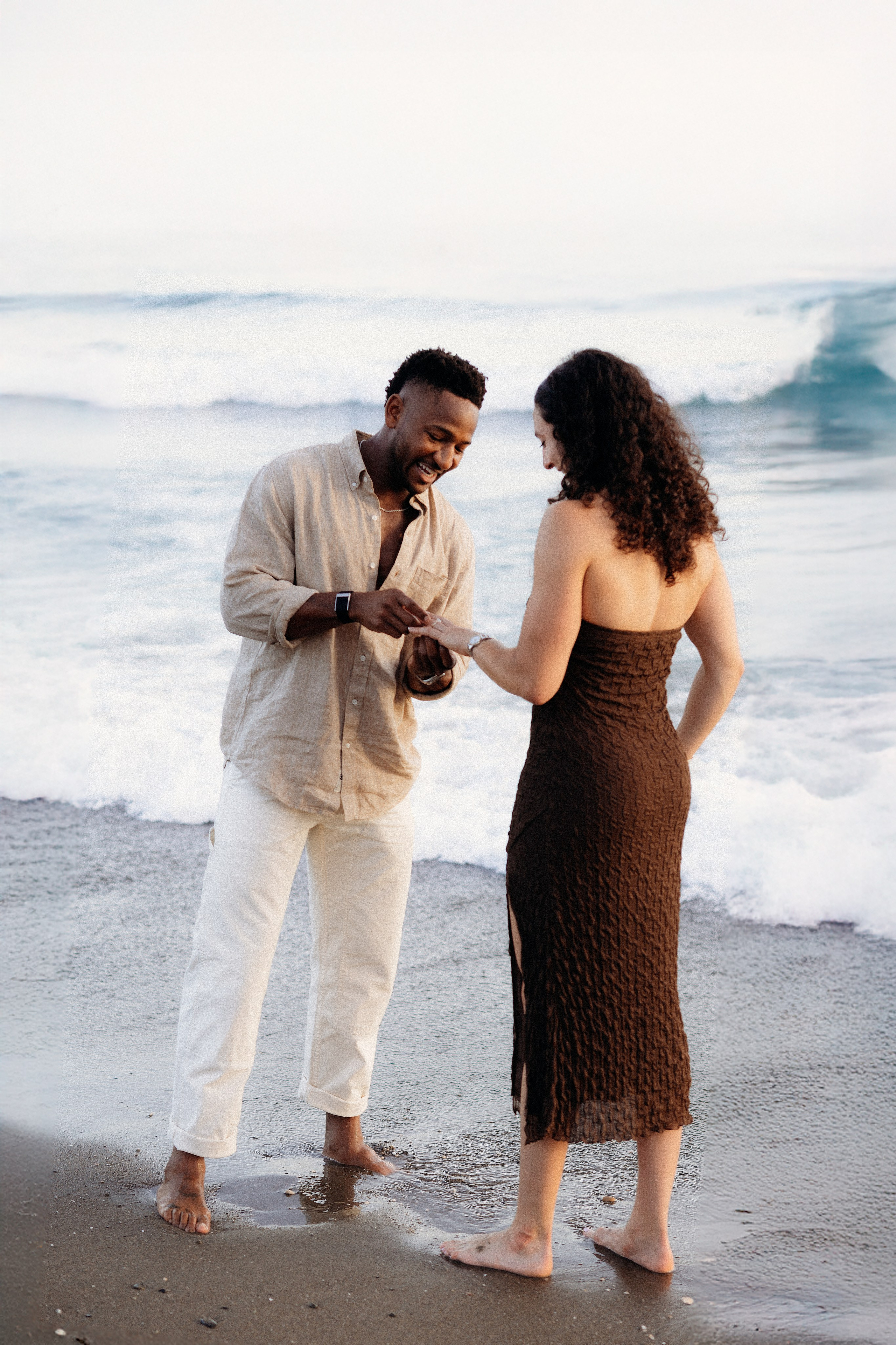 Couple walking barefoot along Málaga beach shoreline during romantic sunset engagement session by the Mediterranean Sea.