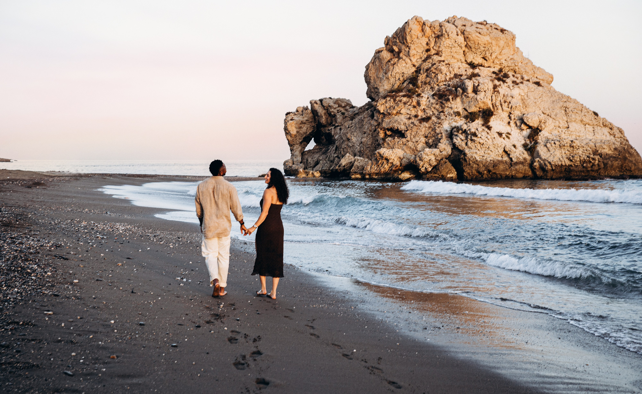 Newly engaged couple walking hand in hand along a Málaga beach after a surprise destination proposal. Coastal engagement photography in southern Spain blending ocean waves, golden sand, and authentic romantic storytelling.