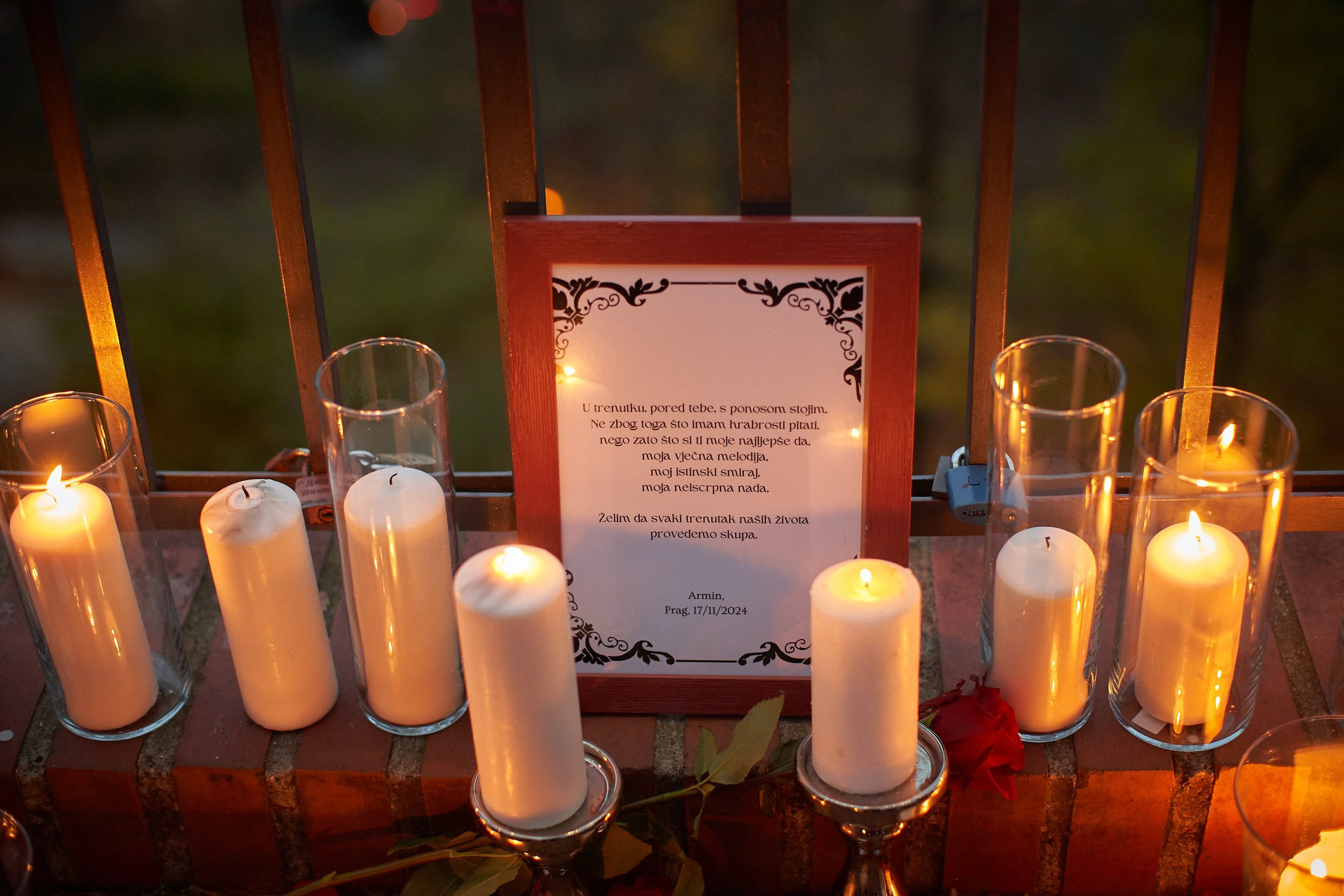 Red framed Bosnian poem surrounded by candles at Prague marriage proposal location at night.