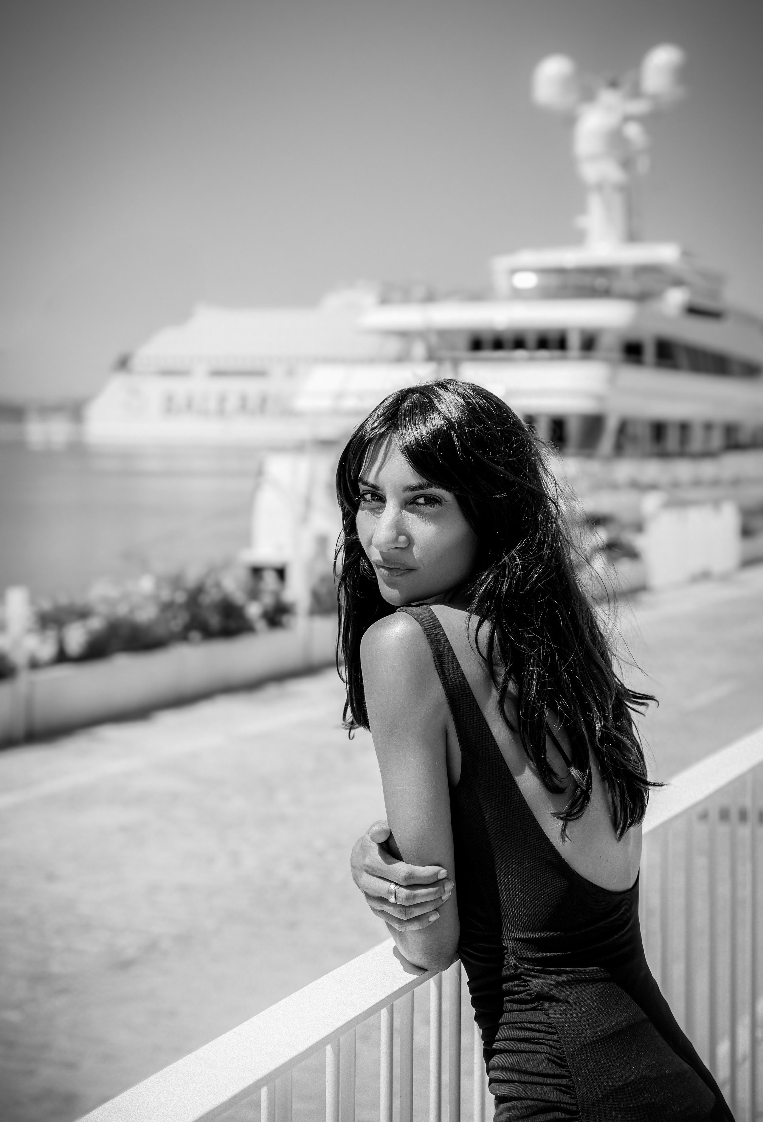 Стильная женщина в черном платье опирается на перила у моря, на фоне роскошной яхты, снято в Малаге, Испания — черно-белая портретная фотография, сочетающая элегантность, прибрежное очарование и средиземноморскую утонченность, идеально подходит для портретных фотосессий в Малаге и Испании.