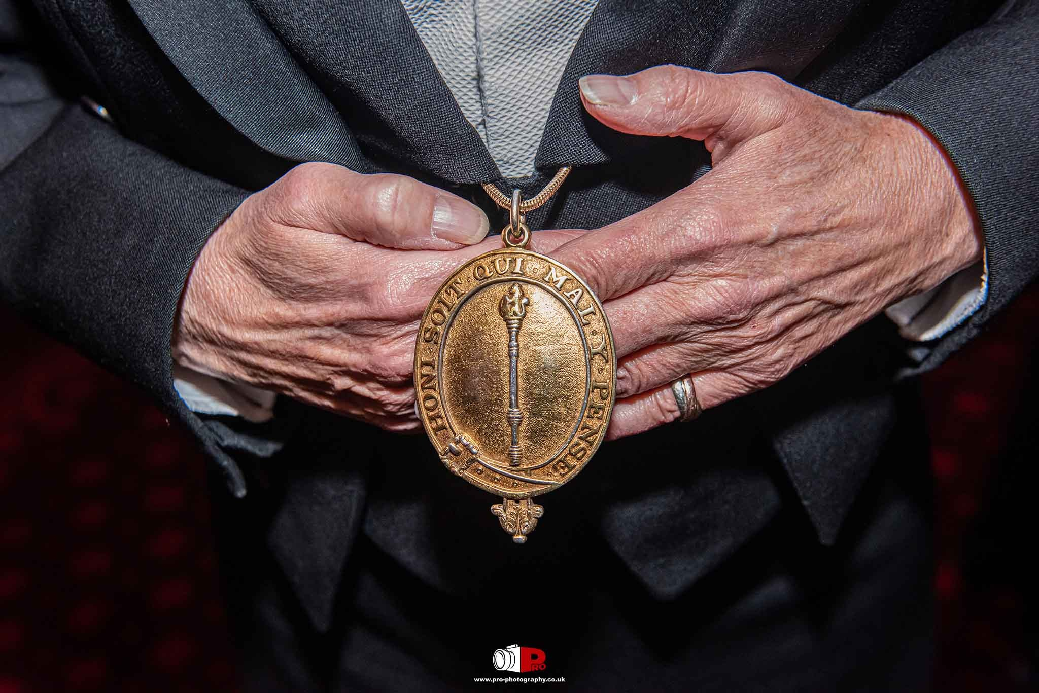 A close-up of a distinguished medal held by a person in a formal suit.