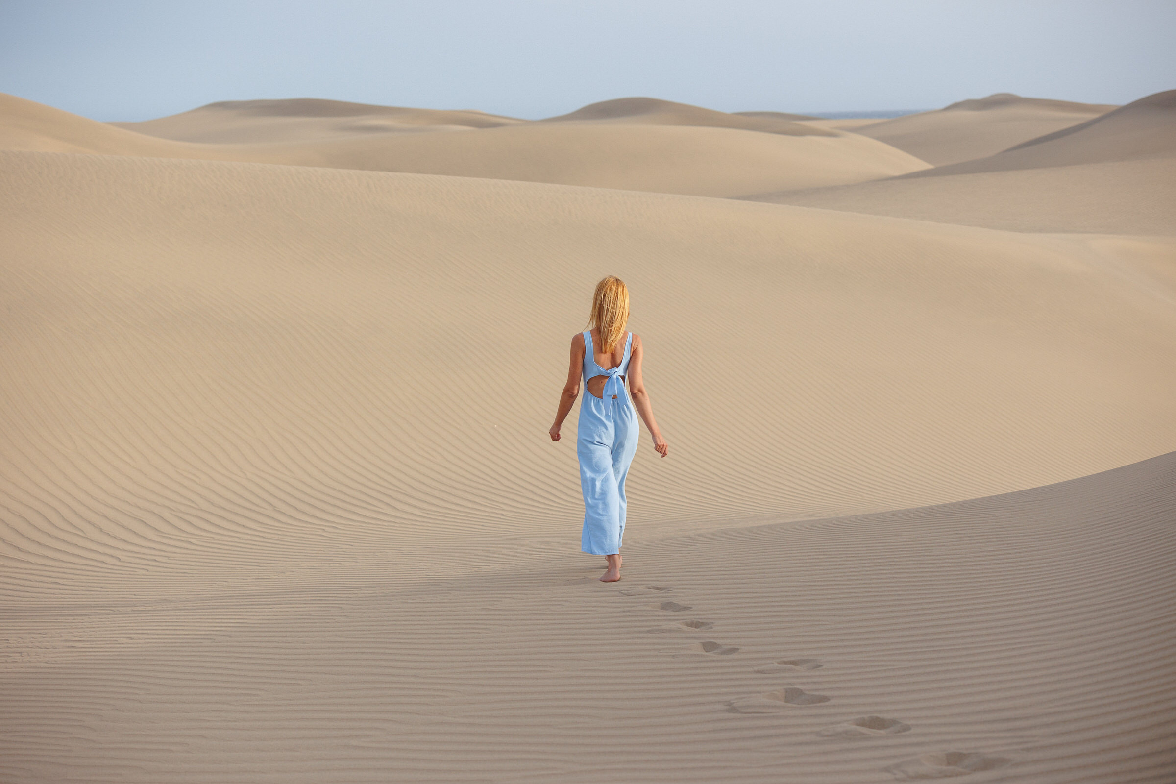 Witness the captivating dance between nature and artistry in Maspalomas de Gran Canaria as our skilled photographer magically captures a young woman's serene walk through the picturesque sand dunes.