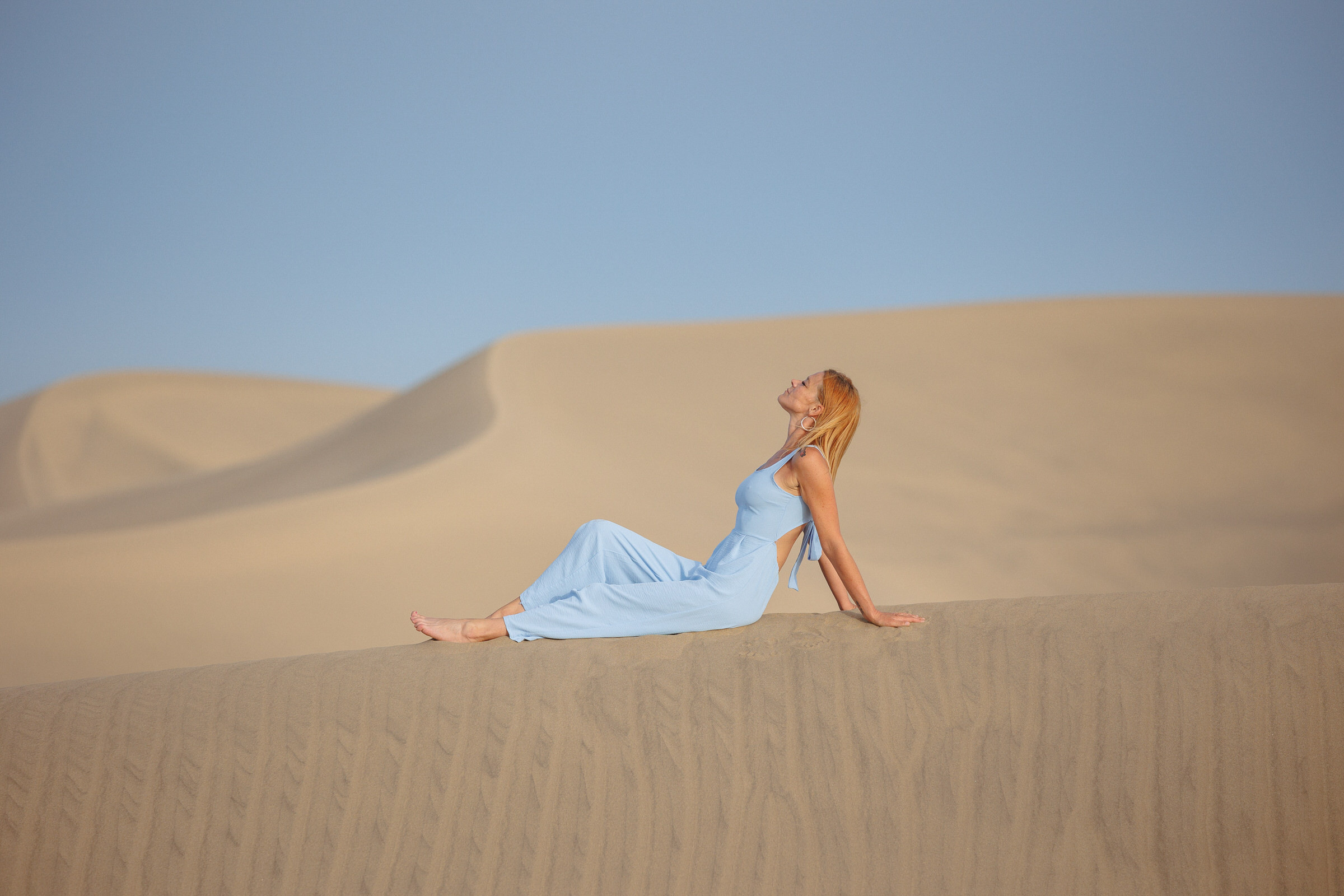 Uncover the artistry of Maspalomas with an extraordinary portrait session. Encounter a captivating woman in a stunning blue dress, serenely seated on a sandy dune.