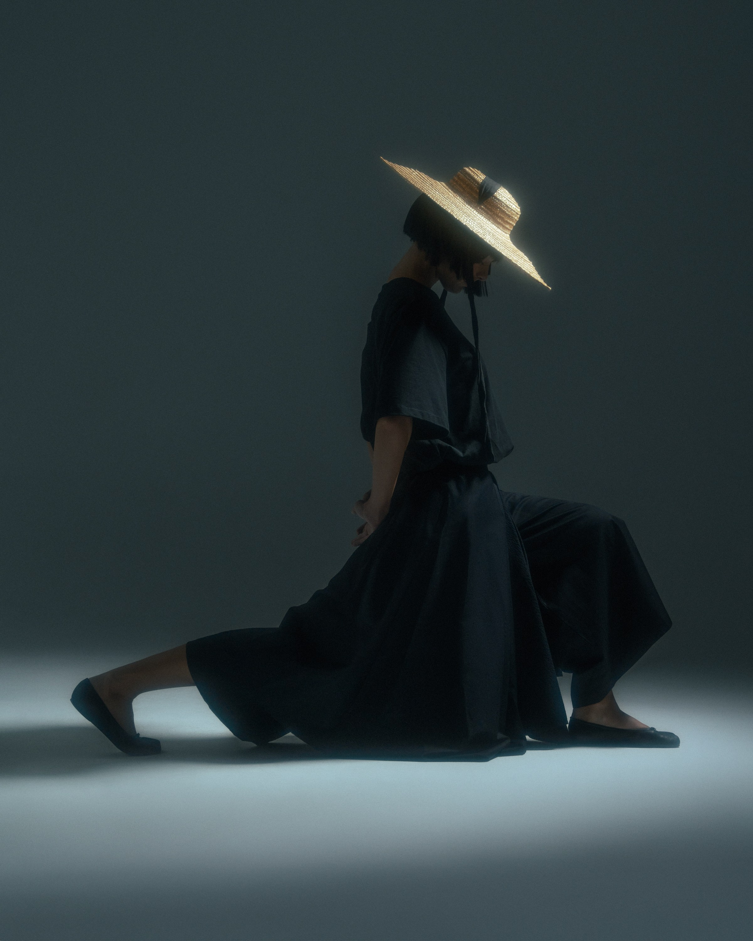 Model in a wide-brimmed hat posing in dramatic studio lighting during a fashion shoot