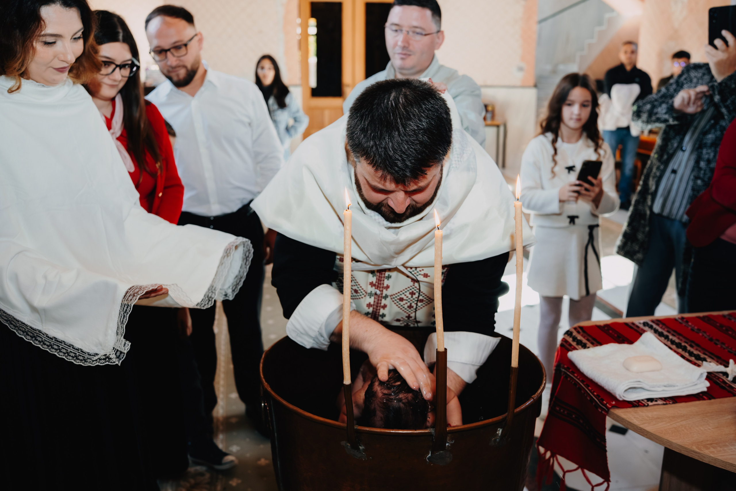 Scăldarea sfântă la botezul lui Arthur Mihail în Catedrala Bârlad. Pruncul este în cristelniță, în timp ce preotul efectuează ritualul, înconjurat de privirile pline de emoție ale familiei și nașilor.