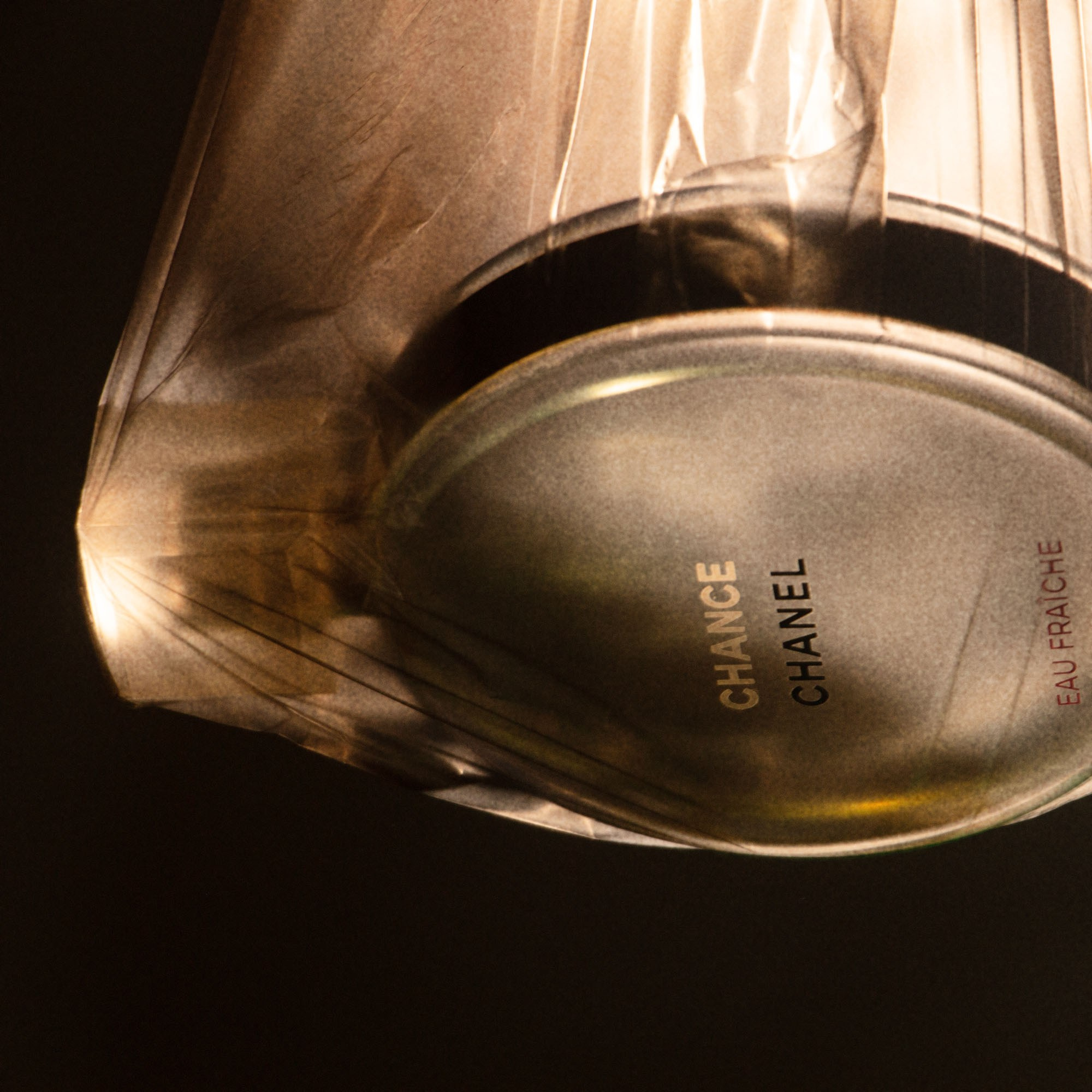 Chanel Chance Eau Fraîche perfume artfully wrapped in transparent film with golden light, symbolizing mystery and exclusivity