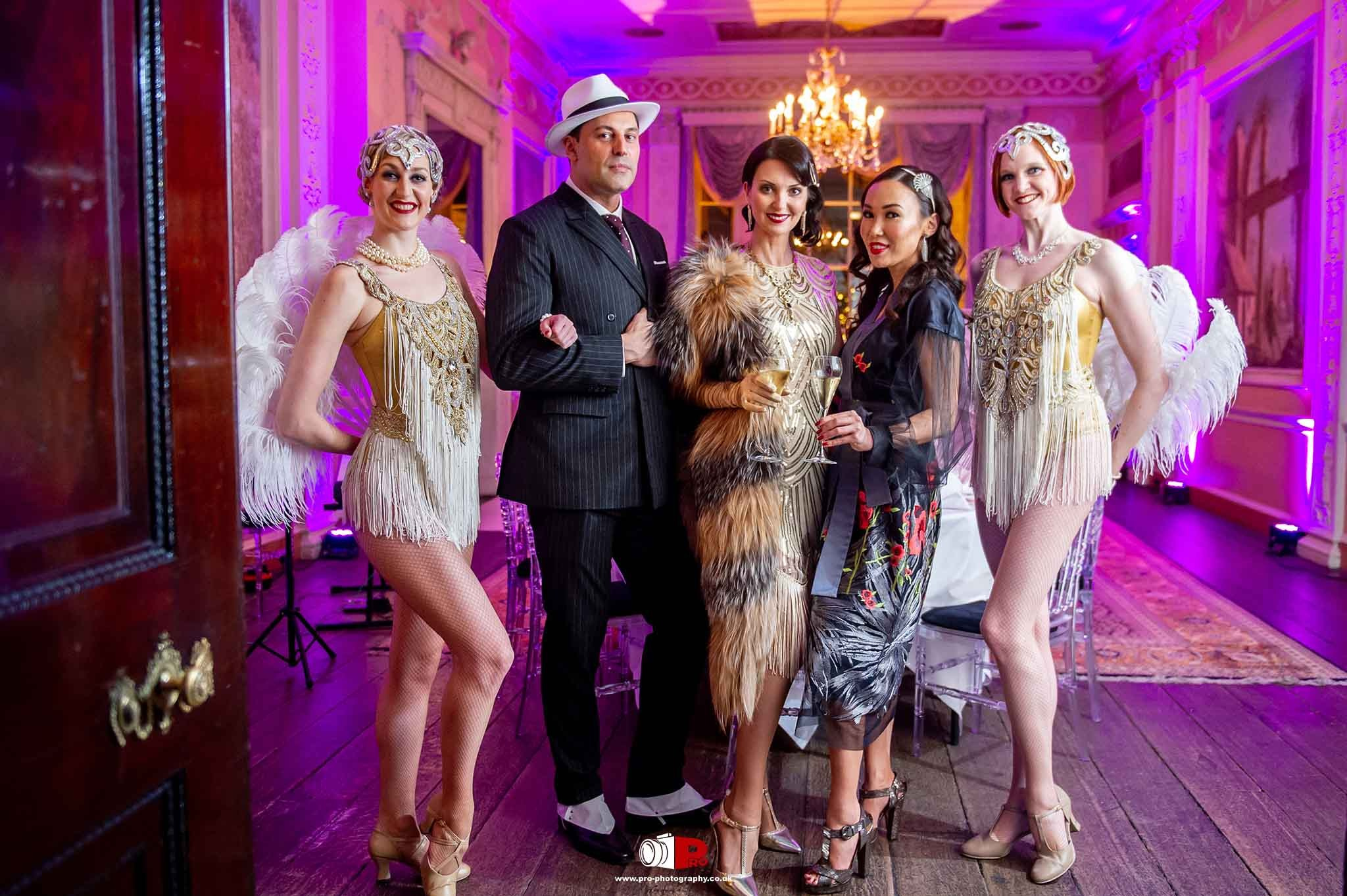 A stylish group of guests in 1920s-inspired outfits posing at an elegant gala venue with vintage decor.