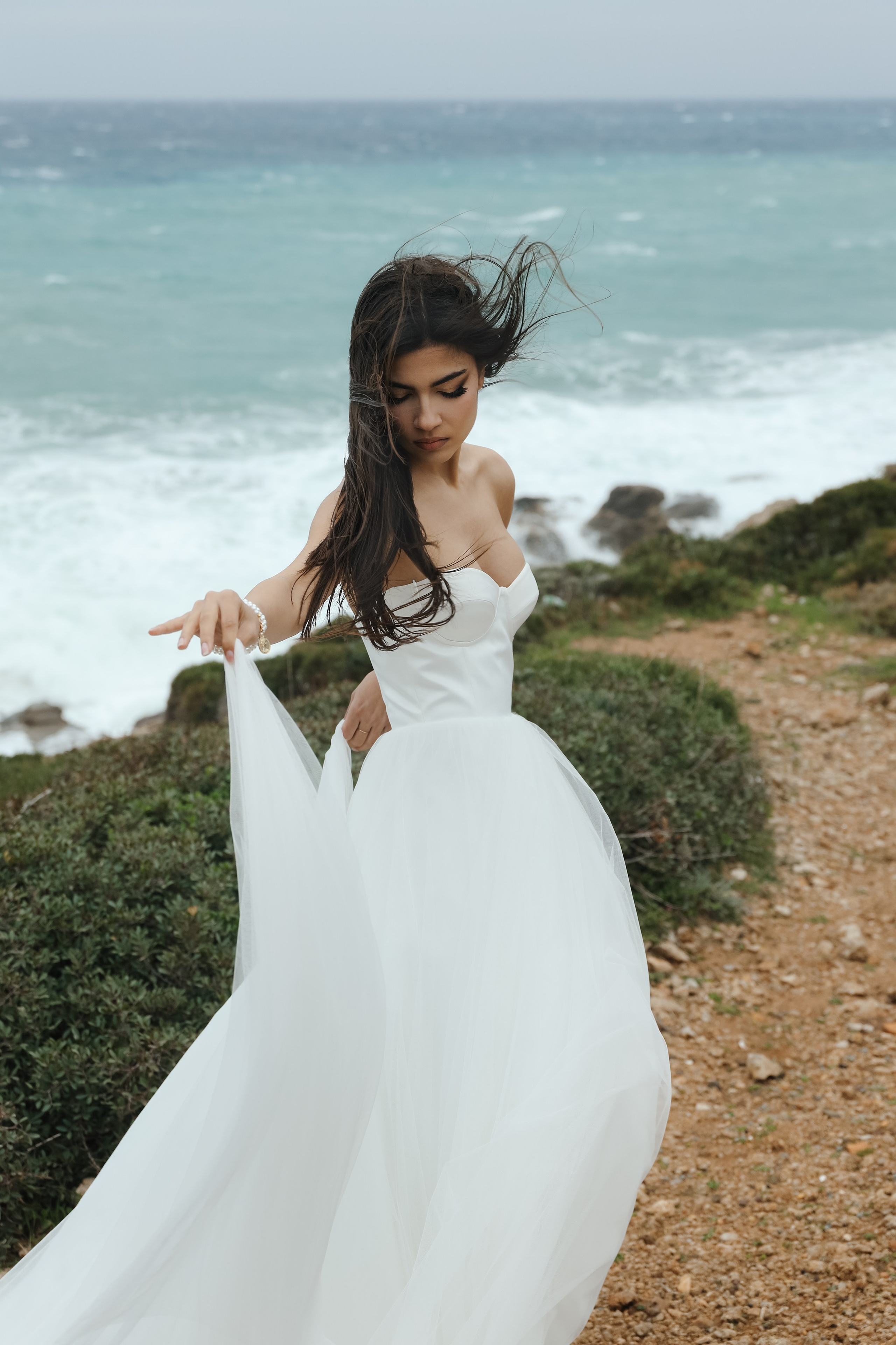 An art photo shoot of a girl in a wedding dress on the windy Kalithea beach in Rhodes, Greece