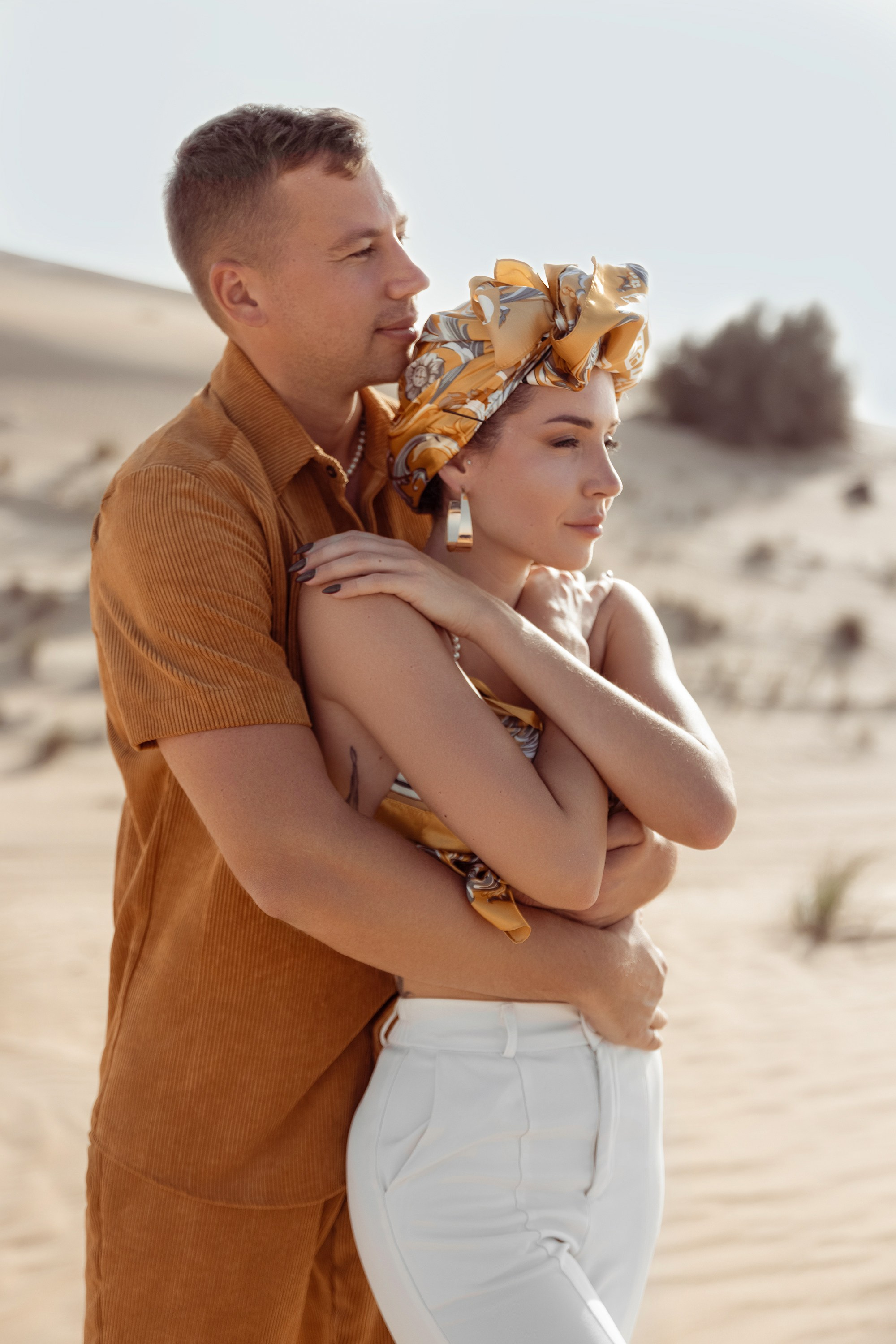 A romantic desert scene: a couple hugs, their silhouettes glowing under the warm sunset light. Dubai, United Arab Emirates