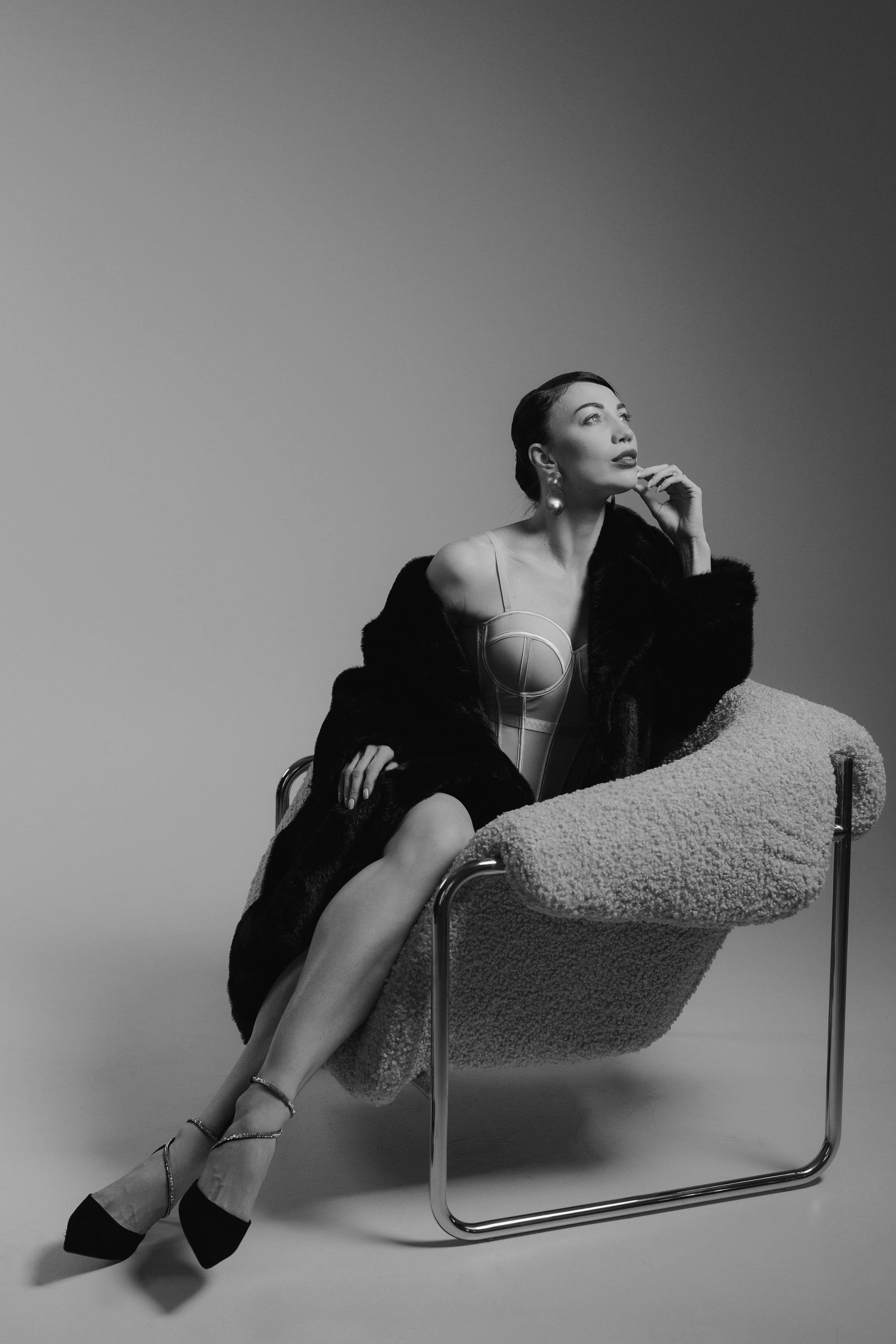 Artistic editorial studio portrait of a woman in a black fur coat sitting in a modern chair with cinematic lighting, photographed in Leipzig, Germany. Художественный редакционный студийный портрет девушки в чёрной шубе, сидящей в современном кресле с кинематографичным светом, снятый в Лейпциге, Германия.