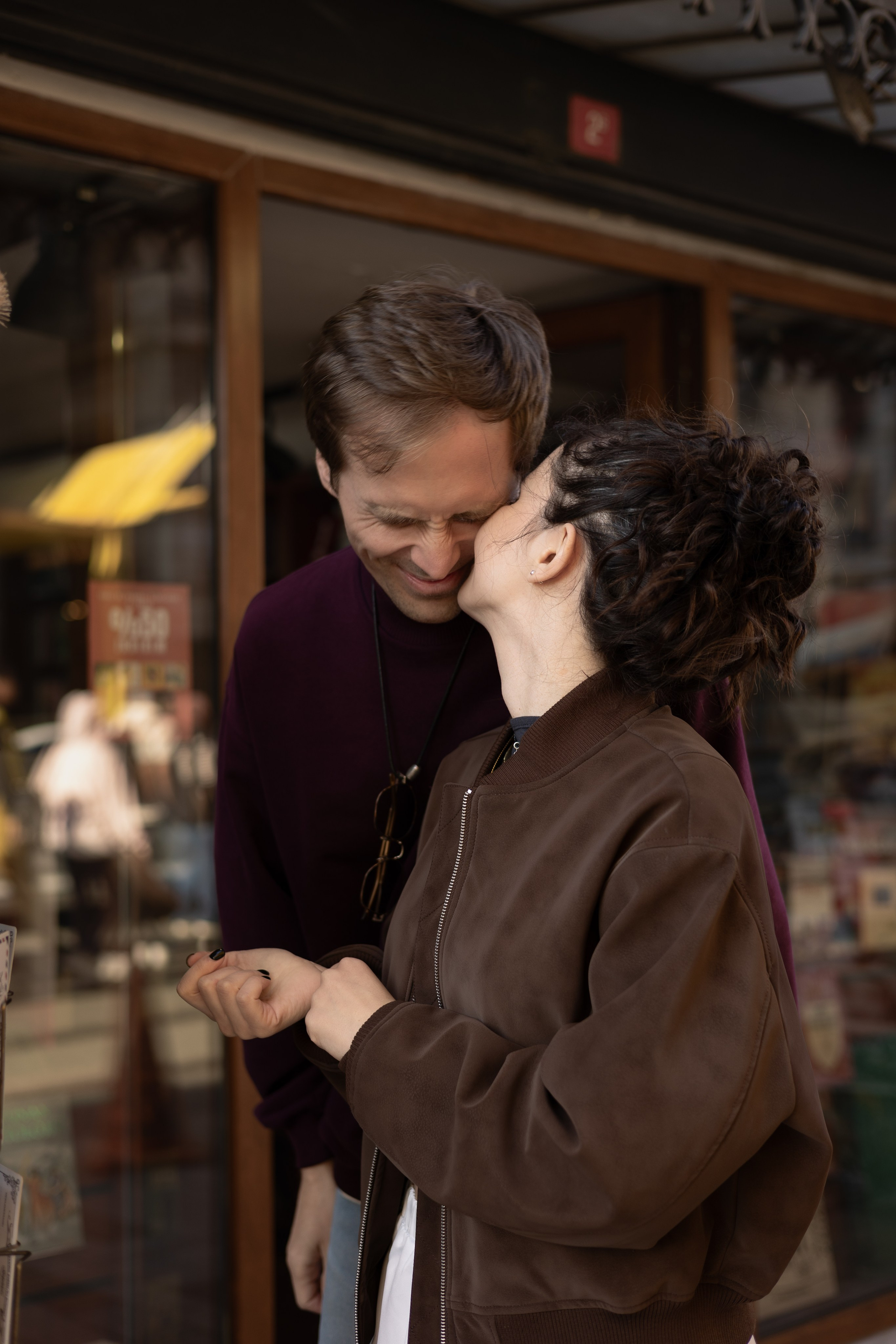 Пара стоит у витрины магазина на городской улице района Пера в Стамбуле, женщина целует мужчину в щёку