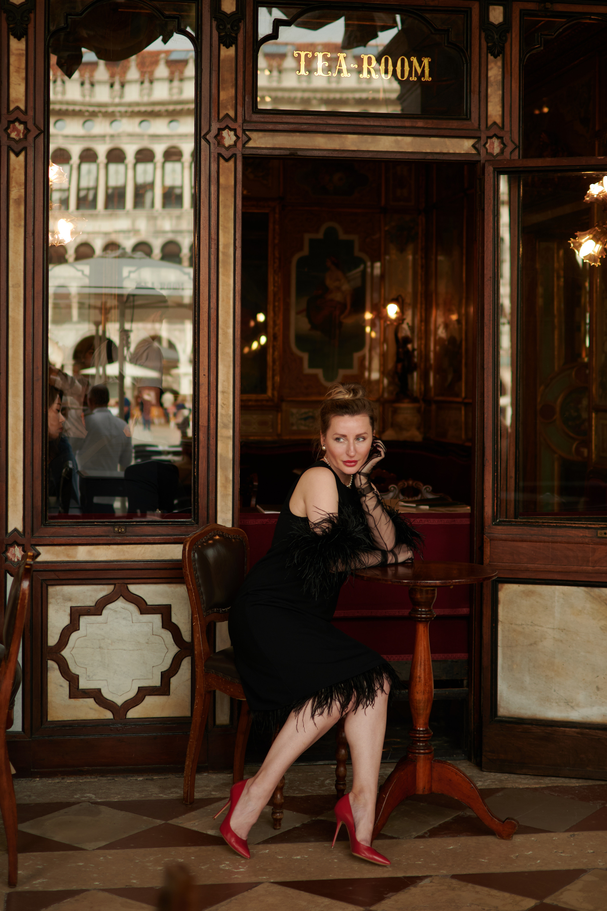 A young woman with a bright smile stands on San Marco square in Venice. She wears a flowing yellow sundress that complements the warm sunlight reflecting off the water behind her. The red and white striped poles of a gondola rest in the background, adding to the Italian charm of the scene. She looks relaxed and carefree, enjoying the beautiful day in this timeless city
