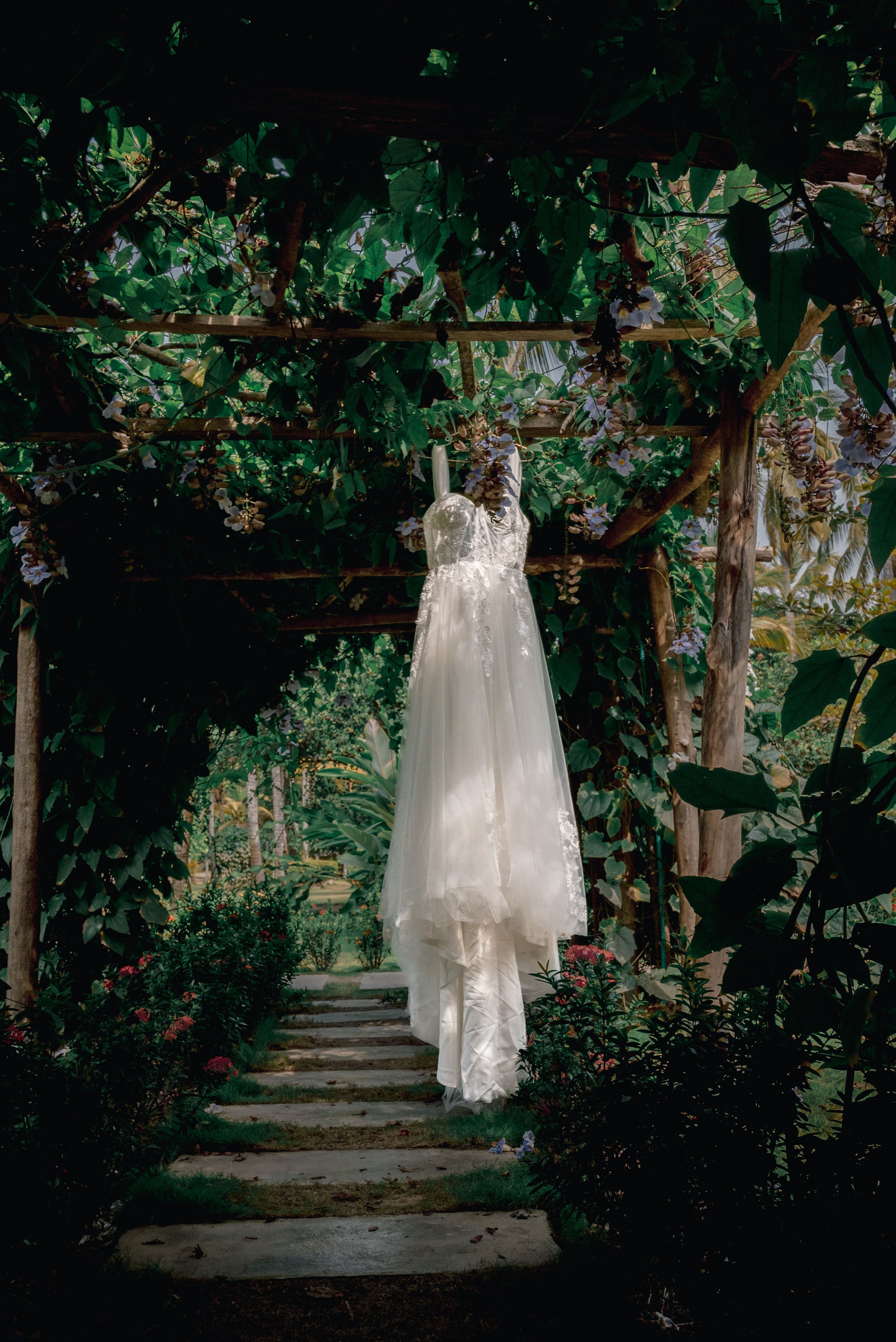 Novia en vestido blanco con velo largo en jardín con vegetación verde, ceremonia de boda en Playa Mareygua Santa Marta