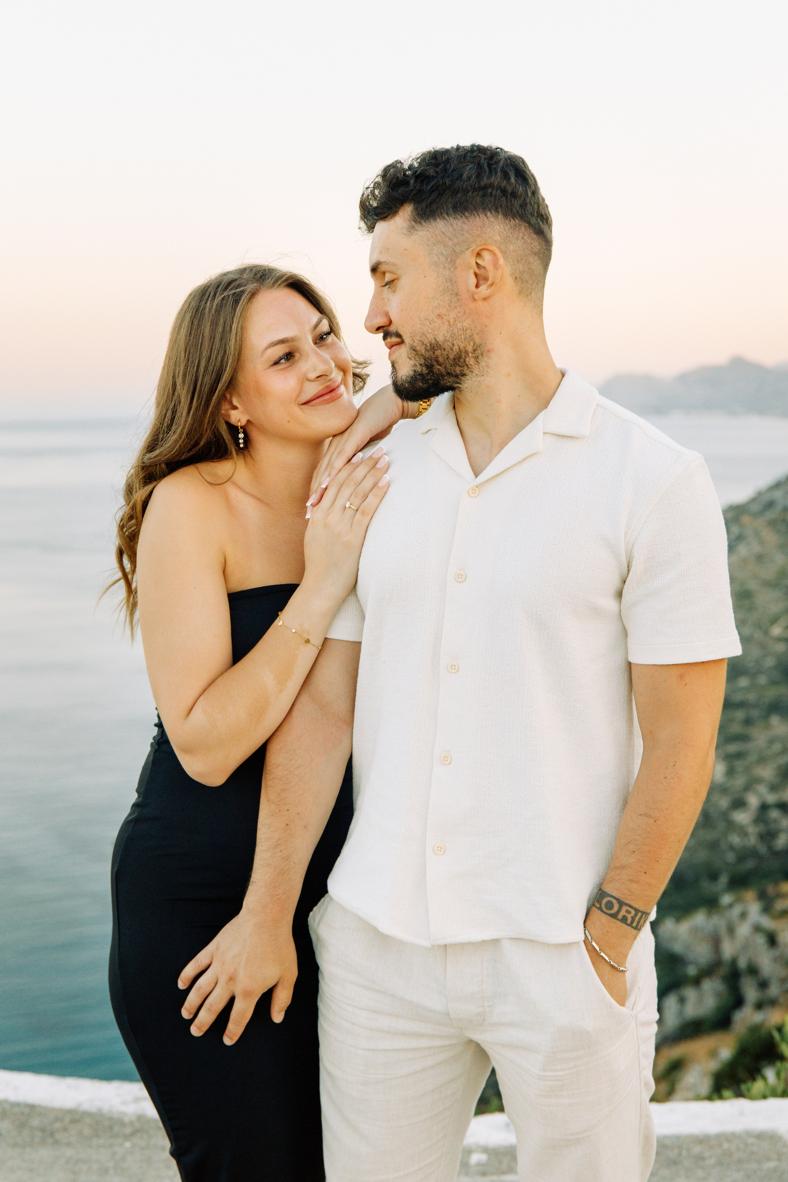 "Liebevoller Blickkontakt: Ein Paar auf dem Felsplateau des Profitis Ilias vor der Kulisse von Faliraki und dem Mittelmeer."