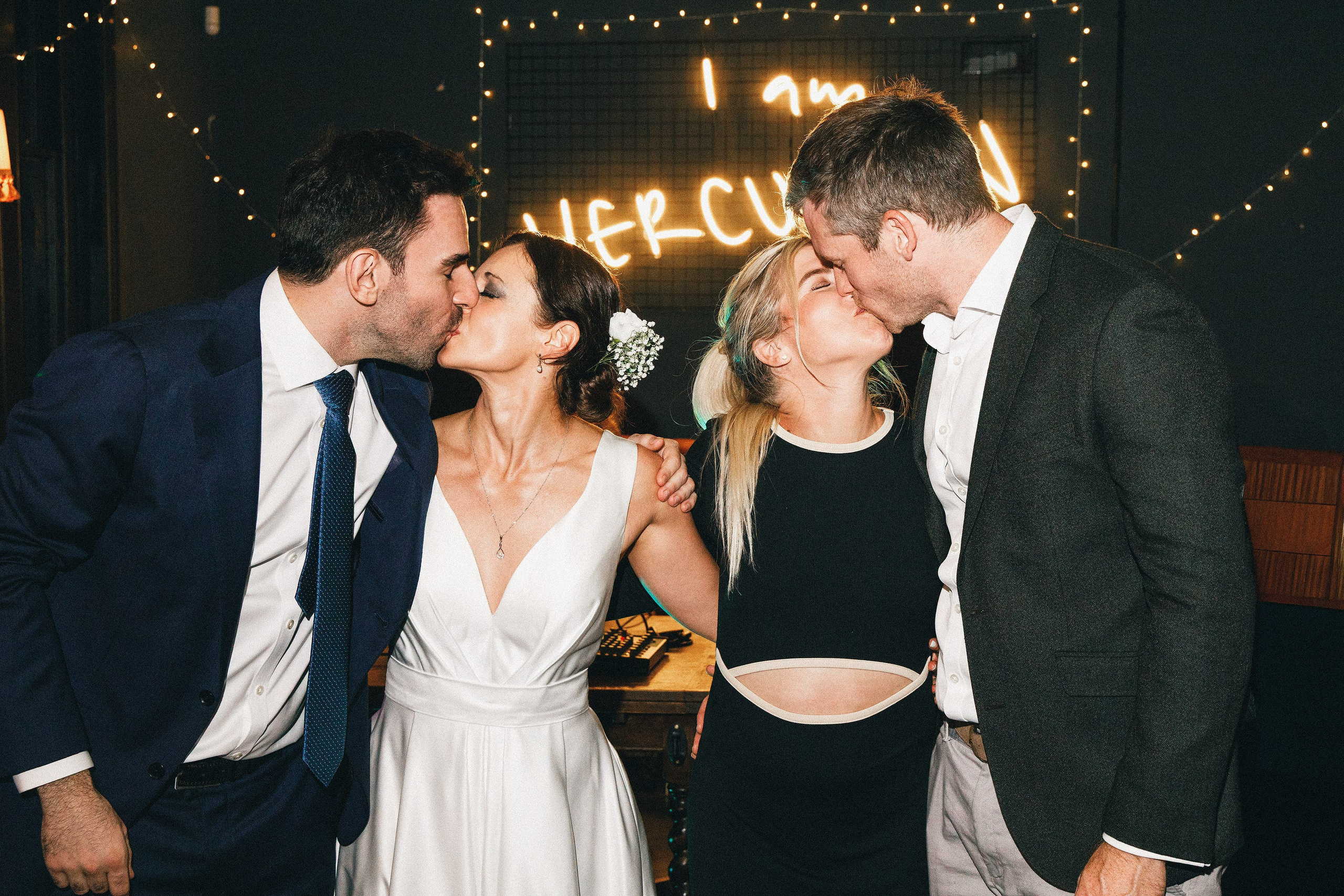 Newlyweds kissing alongside friends at a wedding reception