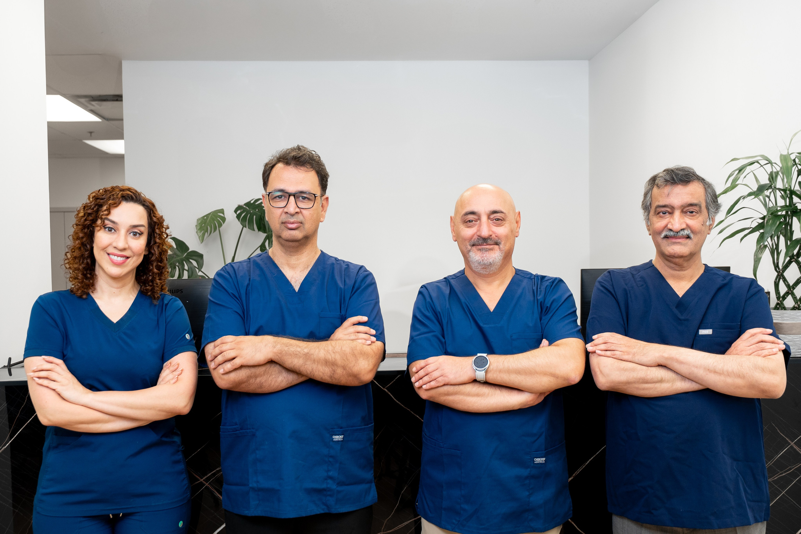 Group portrait of four medical professionals in navy blue scrubs, standing with arms crossed and smiling confidently.