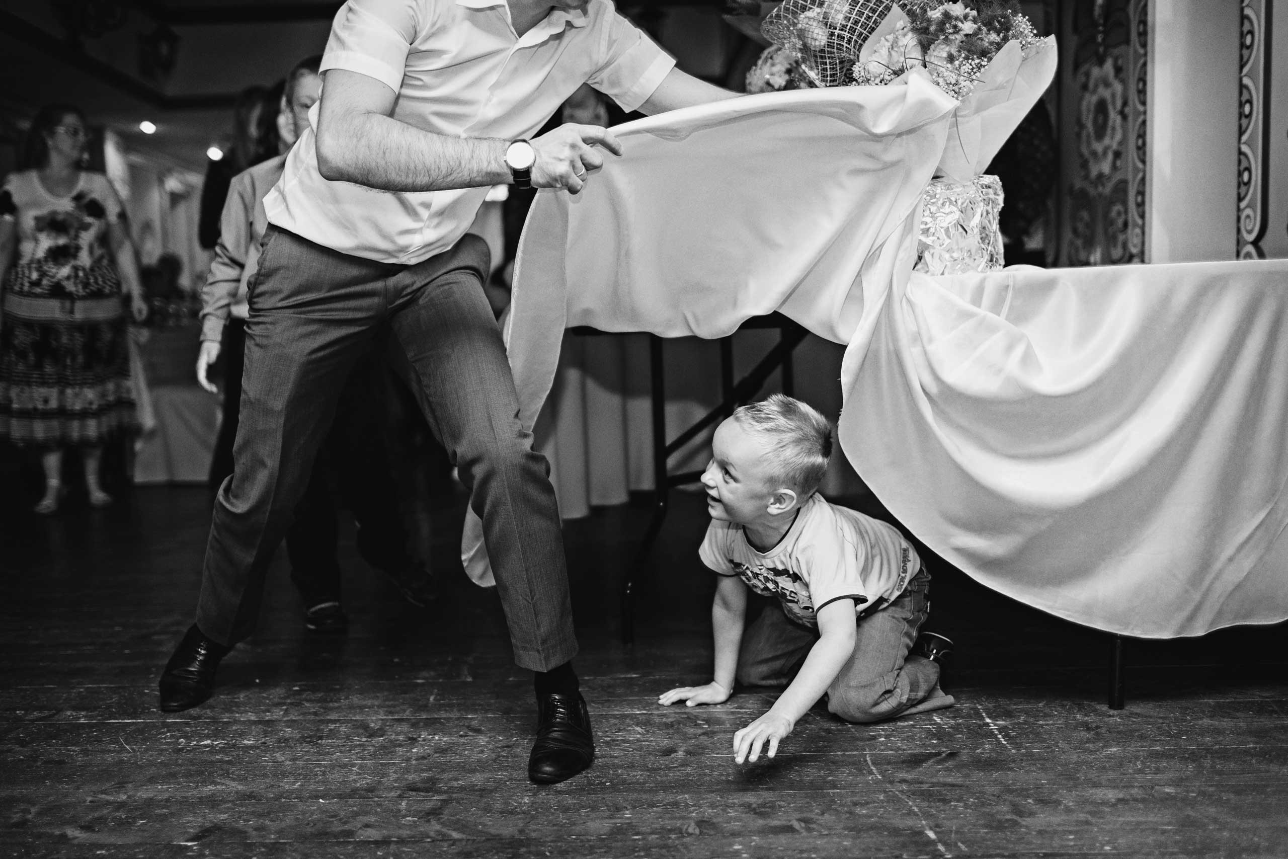 man and a boy hiding under the table are playing at wedding venue