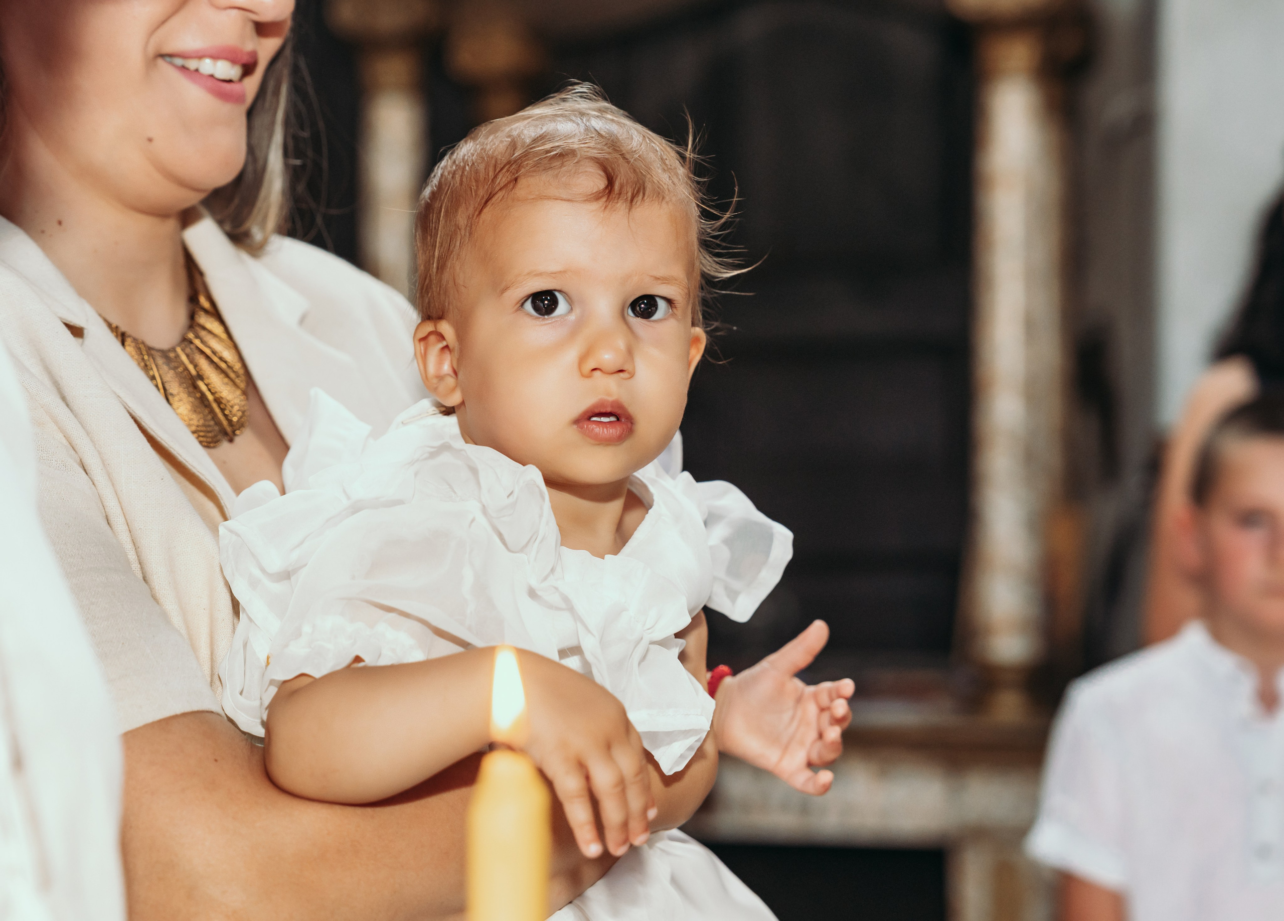 Devojcica u beloj haljini gleda u svecu na krstenju u Beogradu