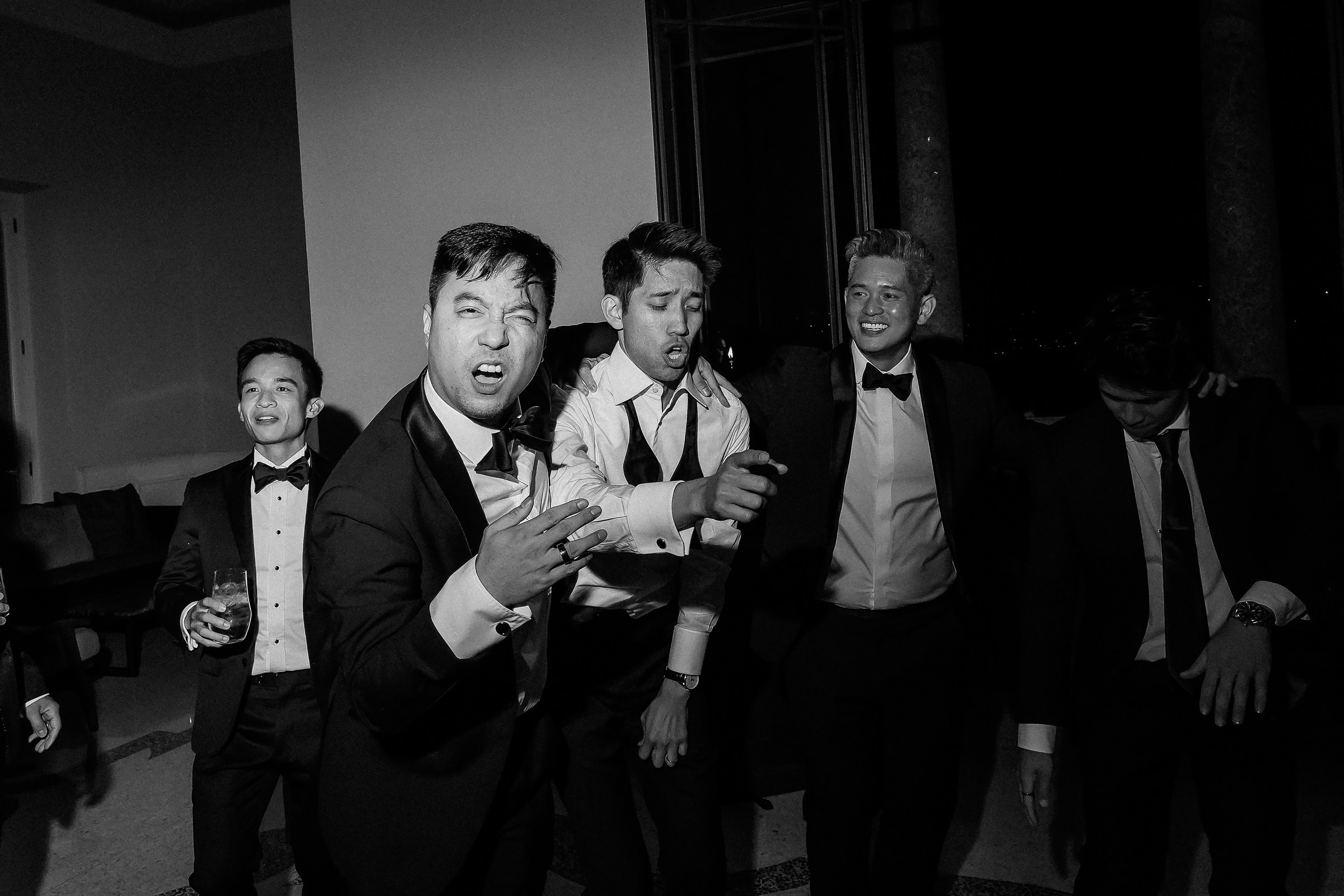 Group of men in suits dancing energetically at a wedding reception, capturing a lively and joyful moment.