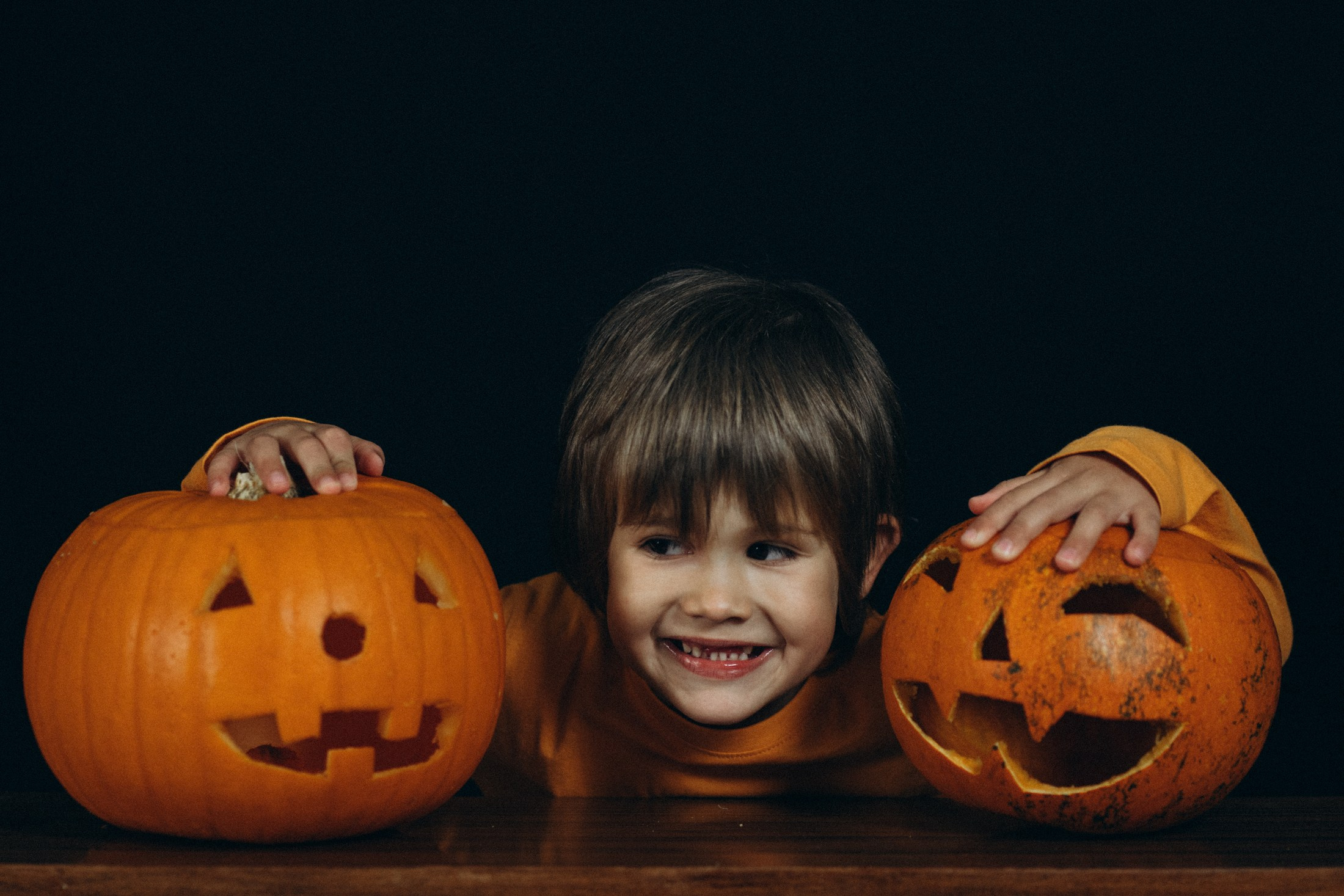 Мальчик улыбается между тыквами-фонарями. Портрет ребенка, Хэллоуин, креативная семейная съемка