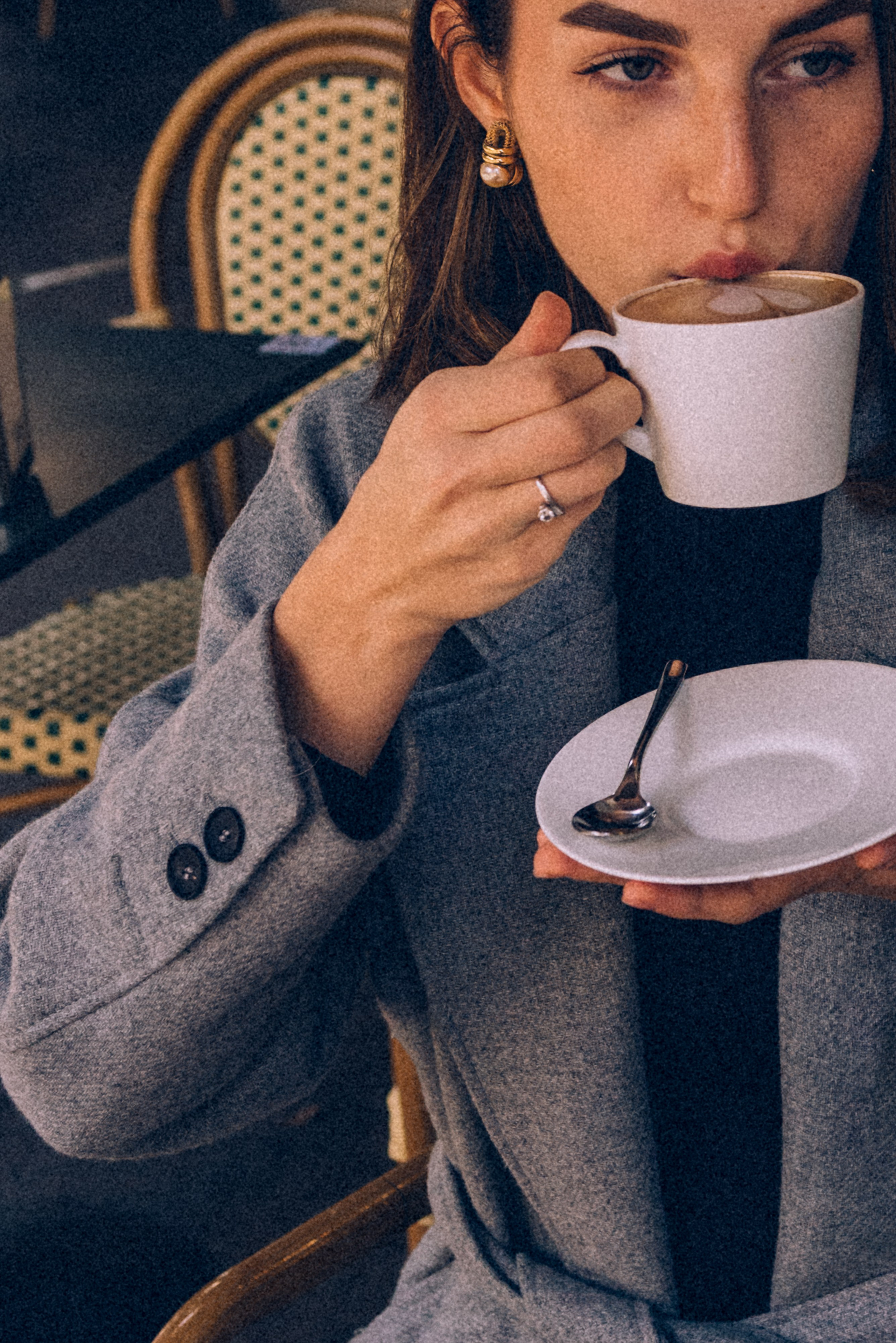Close-up of a stylish woman sipping coffee at an Italian cafe, showcasing understated elegance with gold earrings and a sophisticated gray coat. Milan photographer for tourists