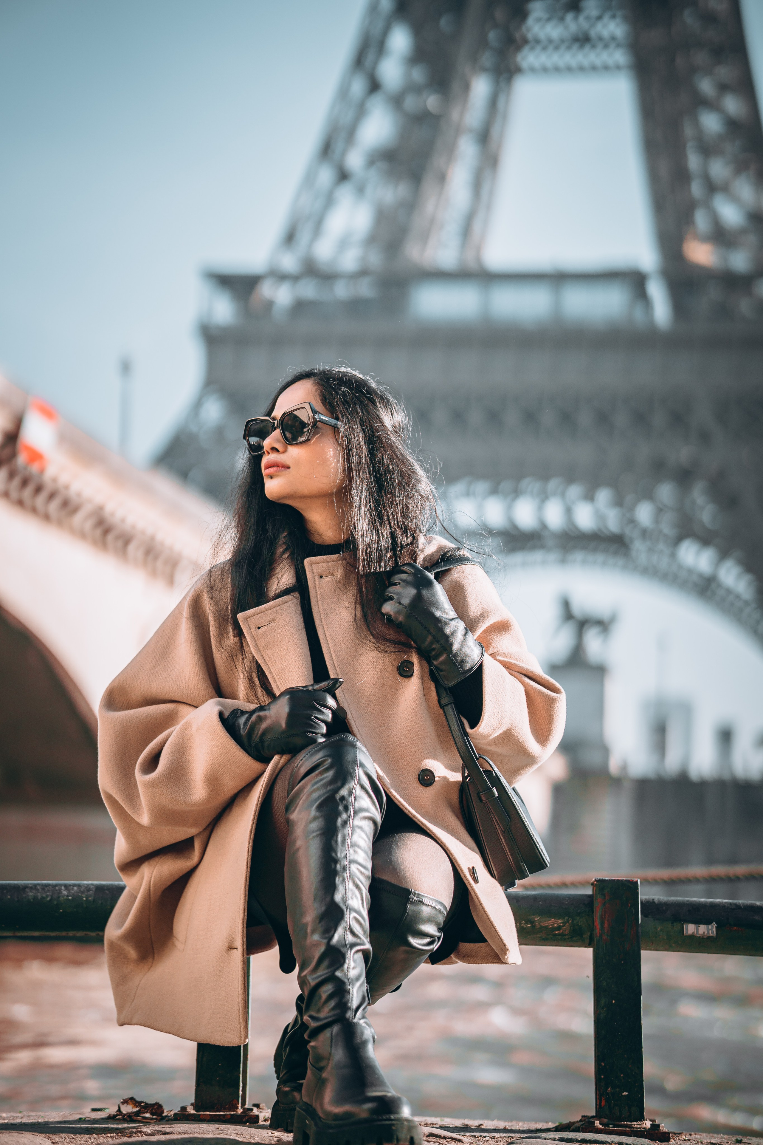 a woman sitting on a rail with paris bridge and eiffel tower behind her