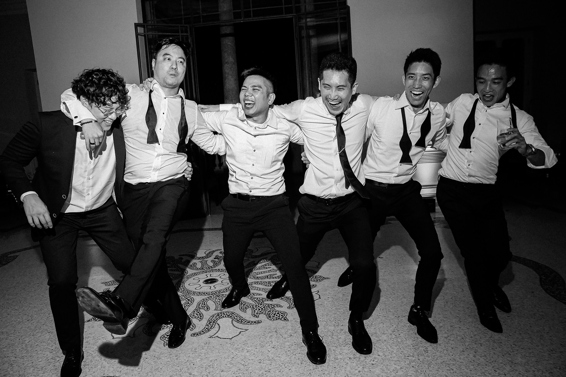 A joyful groom and his groomsmen dance together, celebrating at the wedding reception with laughter and camaraderie. 