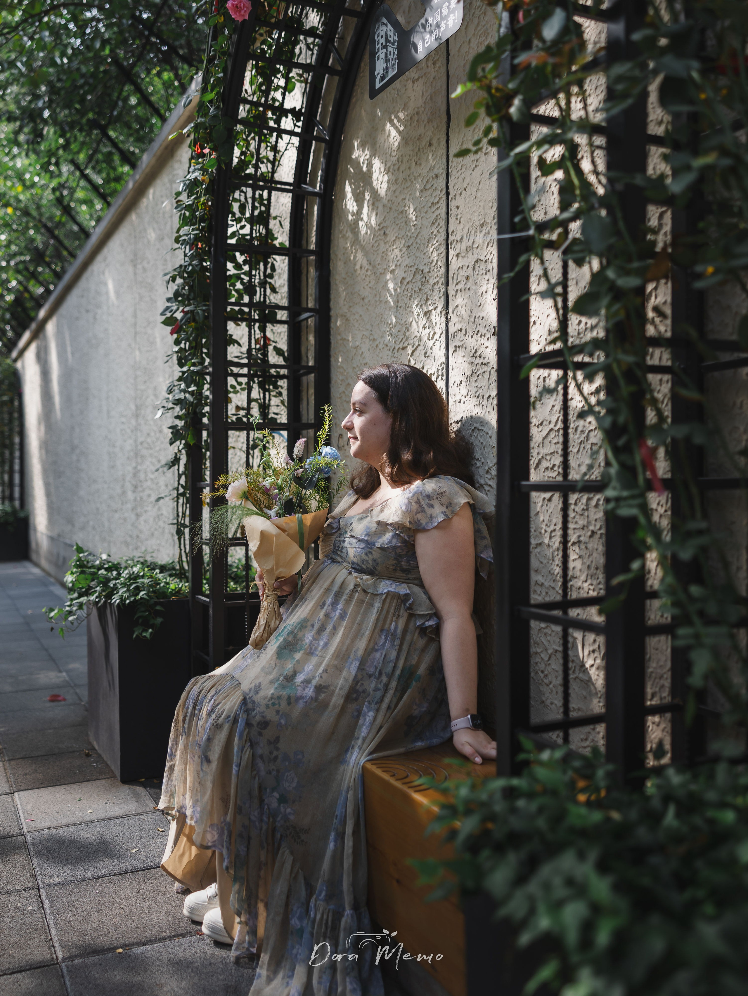 An expecting mother sitting near an old doorway in the Former French Concession with soft greenery around her.