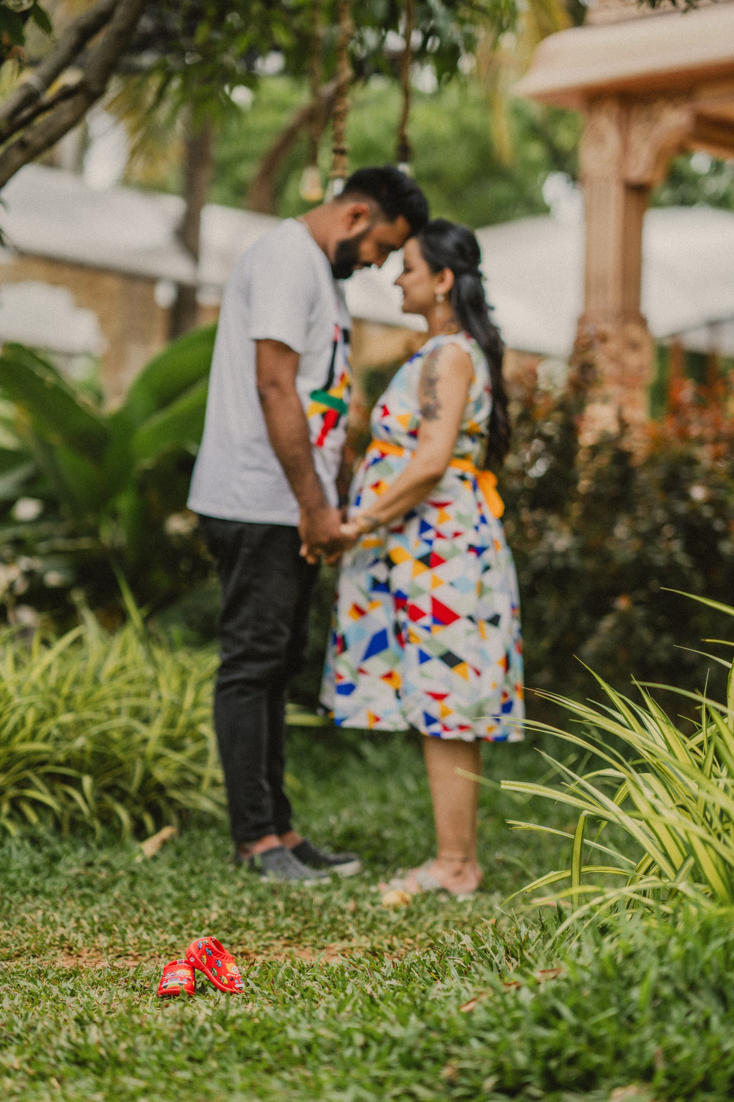Artistic outdoor maternity photoshoot in Bengaluru featuring a blurred couple holding hands in a lush garden.