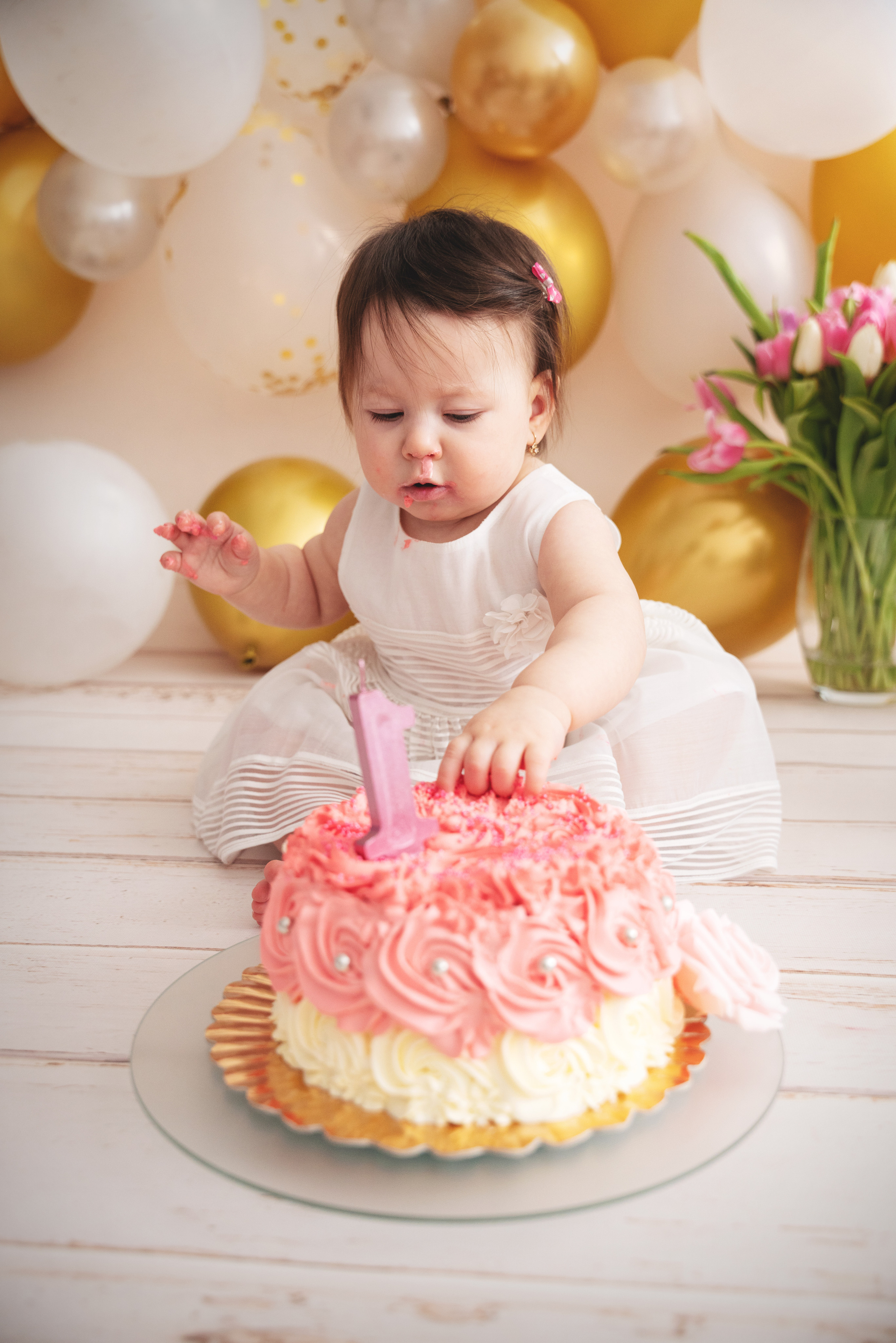 Mädchen feiert den ersten Geburtstag im Studio mit Kuchen und Luftballons