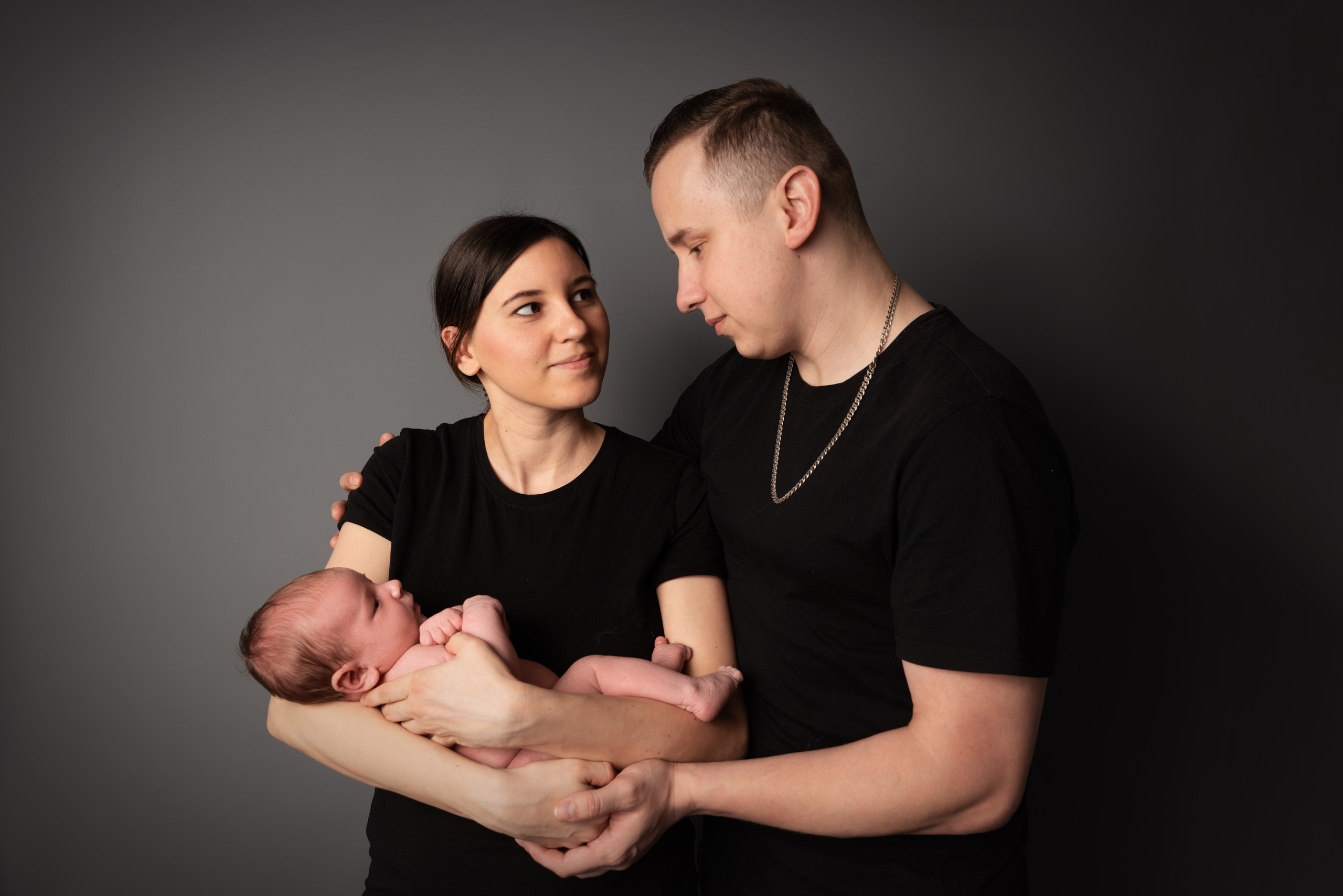 mama hält das Baby und papa umarmt mama und schaut ihr in die augen