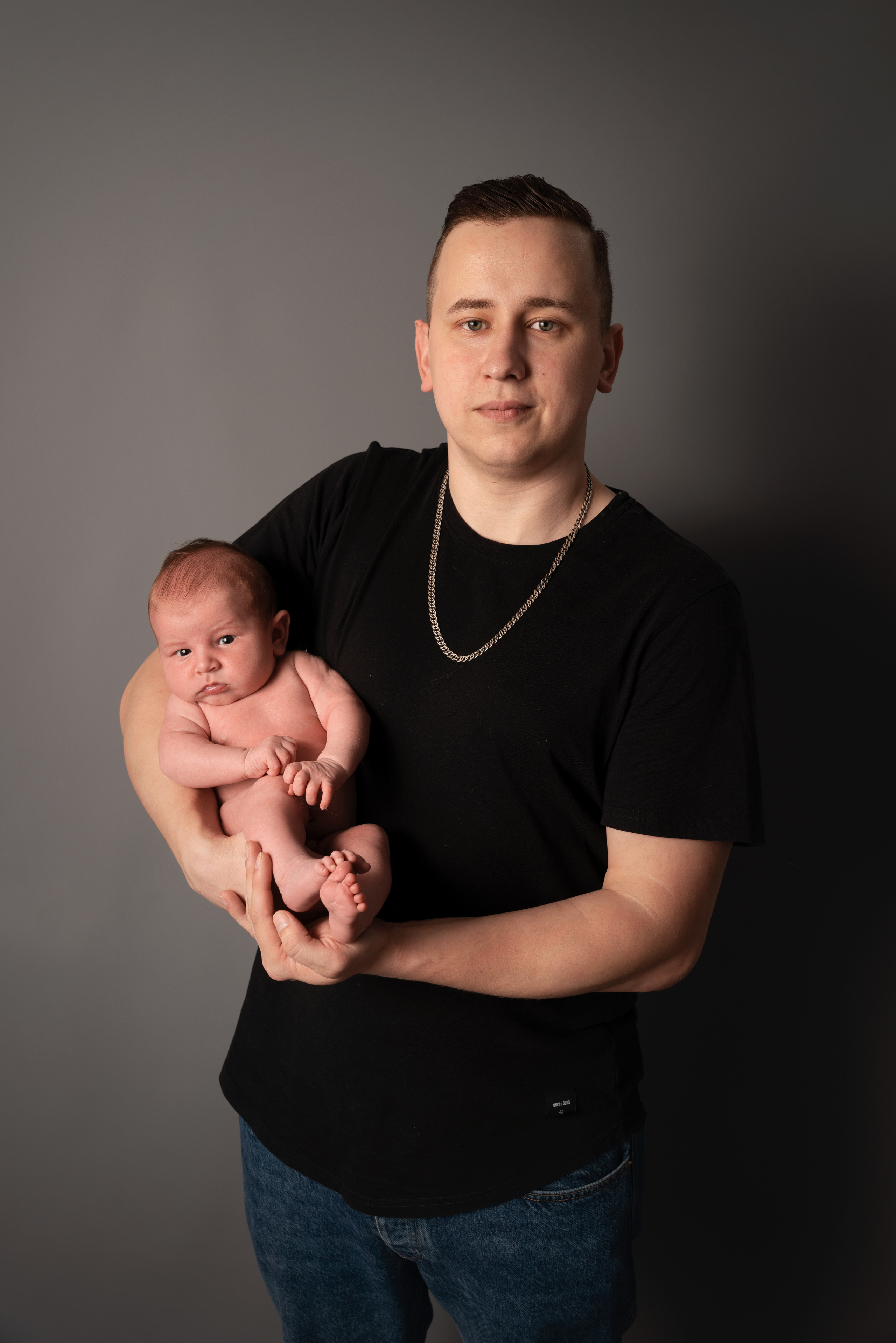 papa hält das baby und sie sehen beide den fotografen an