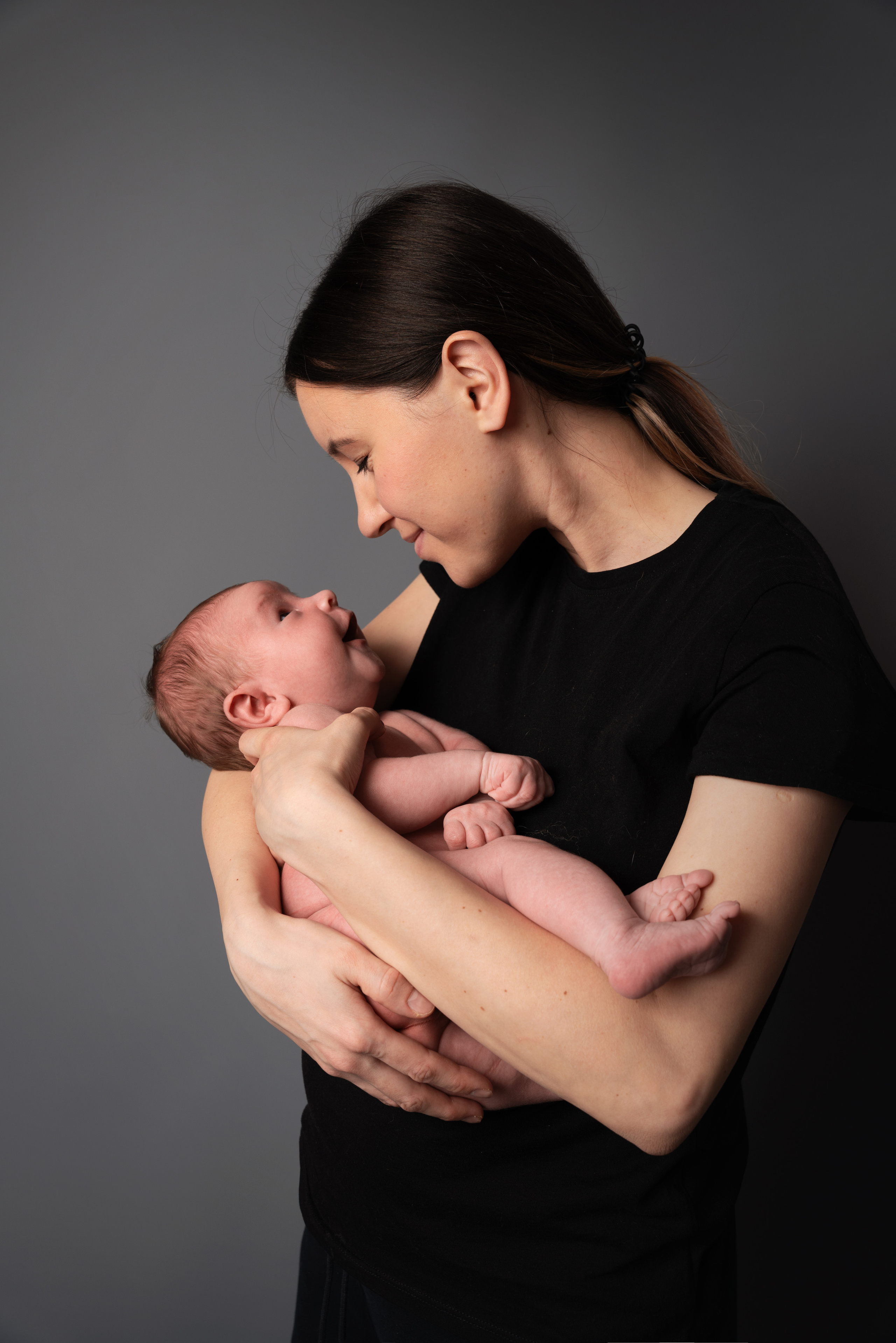 auf grauem Studiohintergrund steht eine Mutter mit einem Baby 